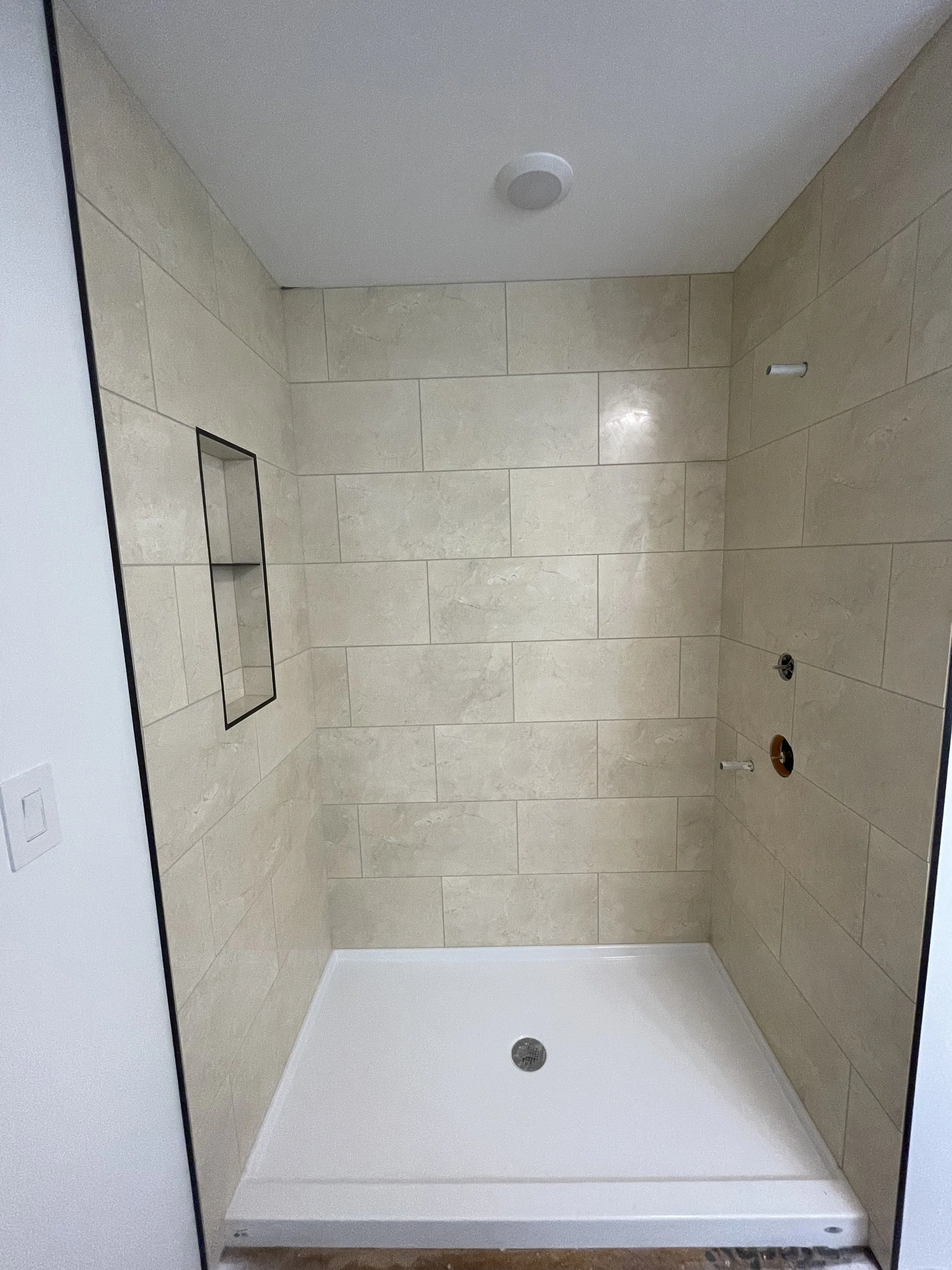 A tiled shower area with beige tiles, a white shower pan, and a wall niche for storage.