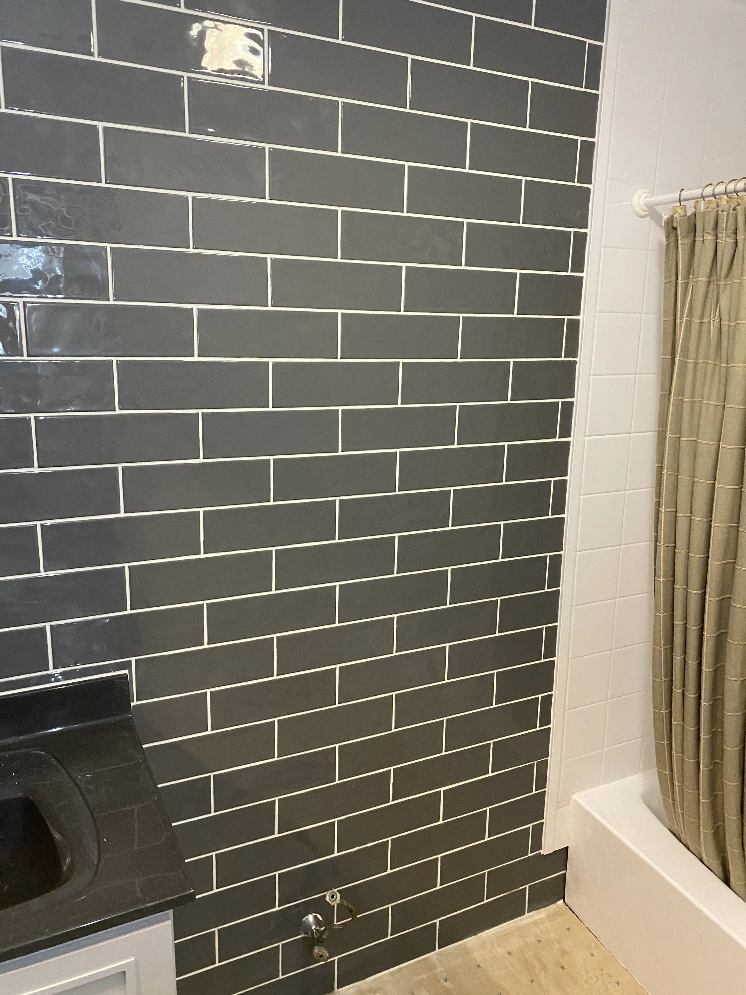 Bathroom with dark gray subway tiles, a black countertop with a sink, and a white bathtub with a beige shower curtain.