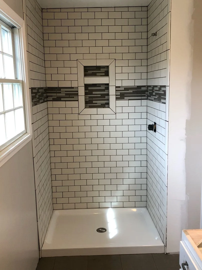Modern shower with white subway tile and decorative strip, recessed shelf, and window.