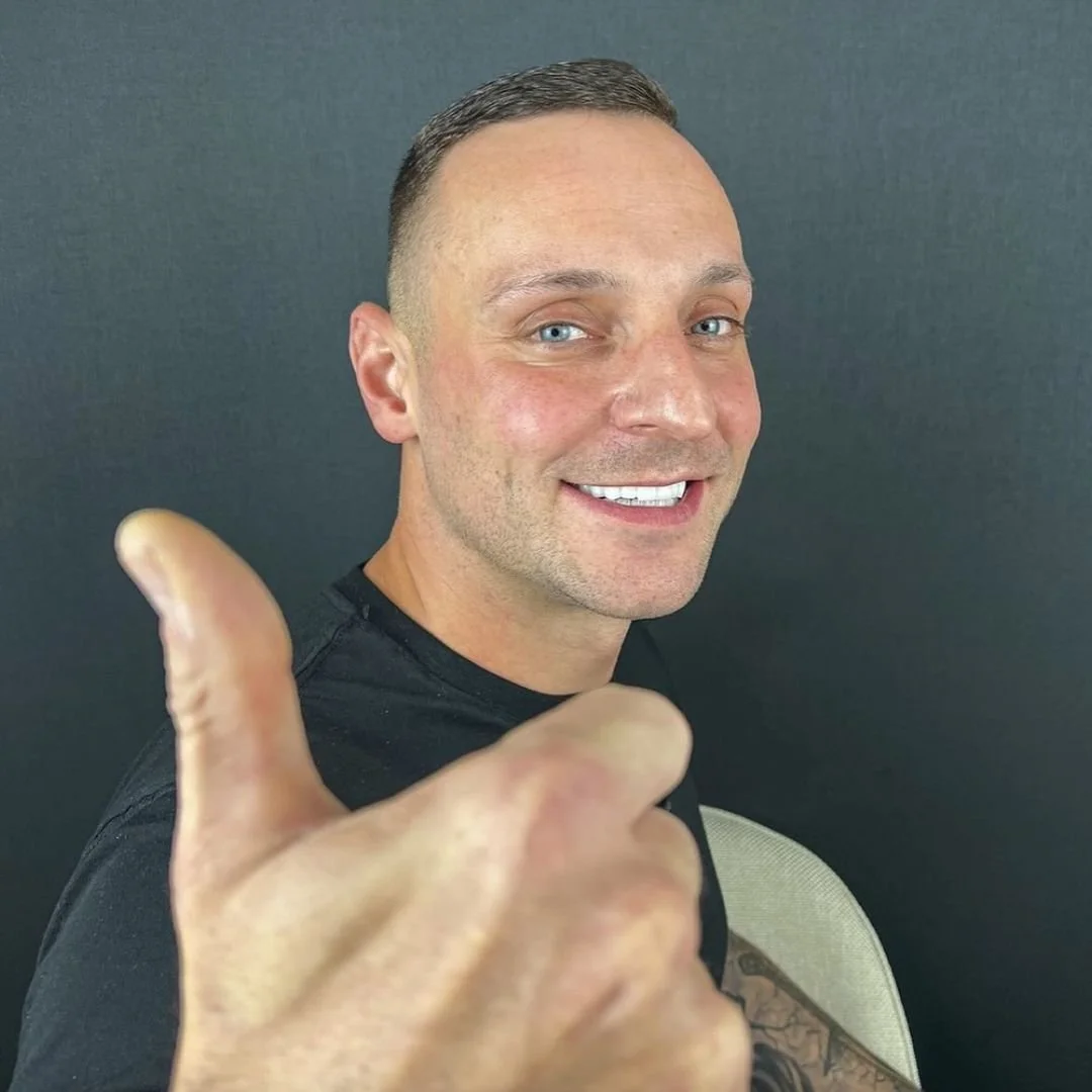 Man smiling with thumb up against a dark background.