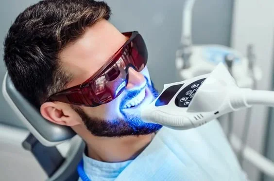 Person undergoing professional teeth whitening treatment with a laser and wearing protective eyewear.