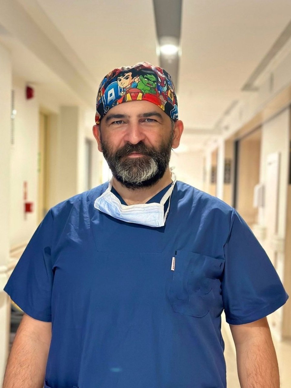 Person in scrubs and surgical cap standing in a hallway.