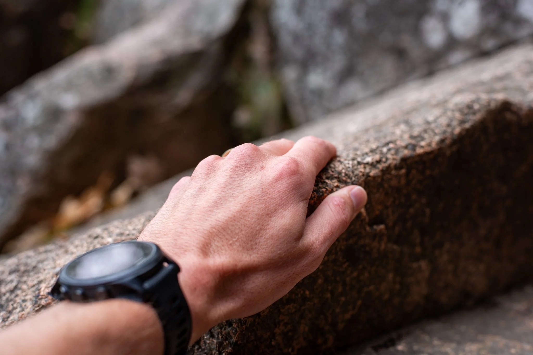 Close-up of a person's hand gripping a rough, textured stone or concrete surface, with a blurred background.