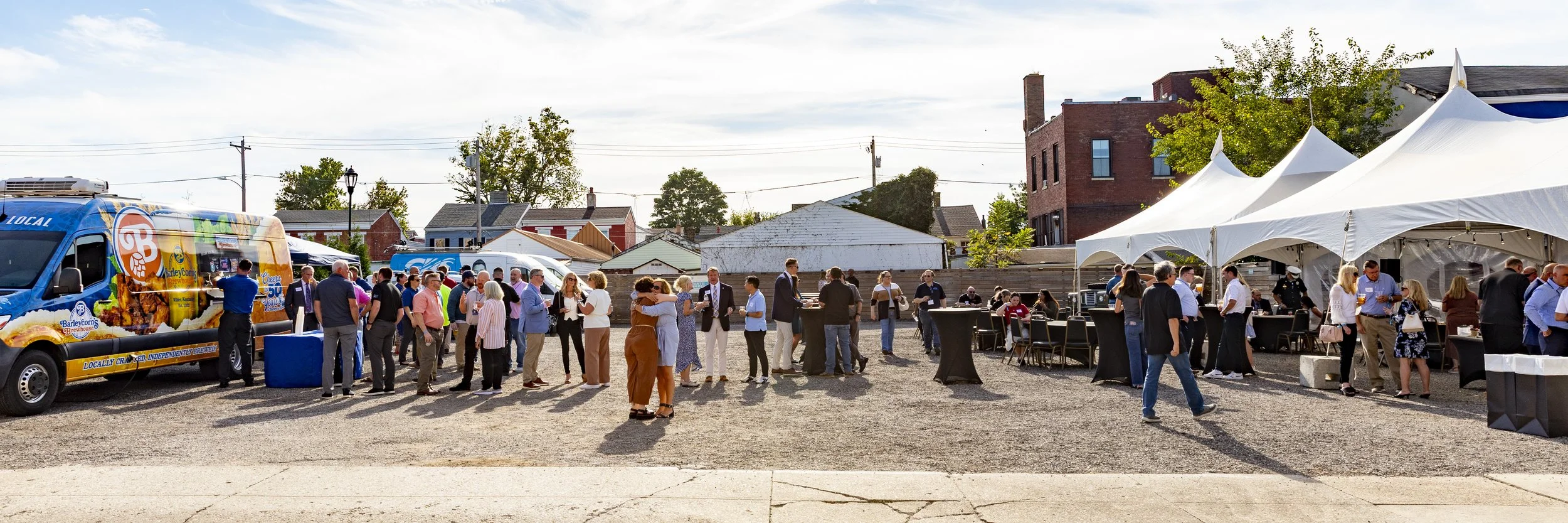 People gathered at an outdoor event with food trucks and white tents in a small urban area.