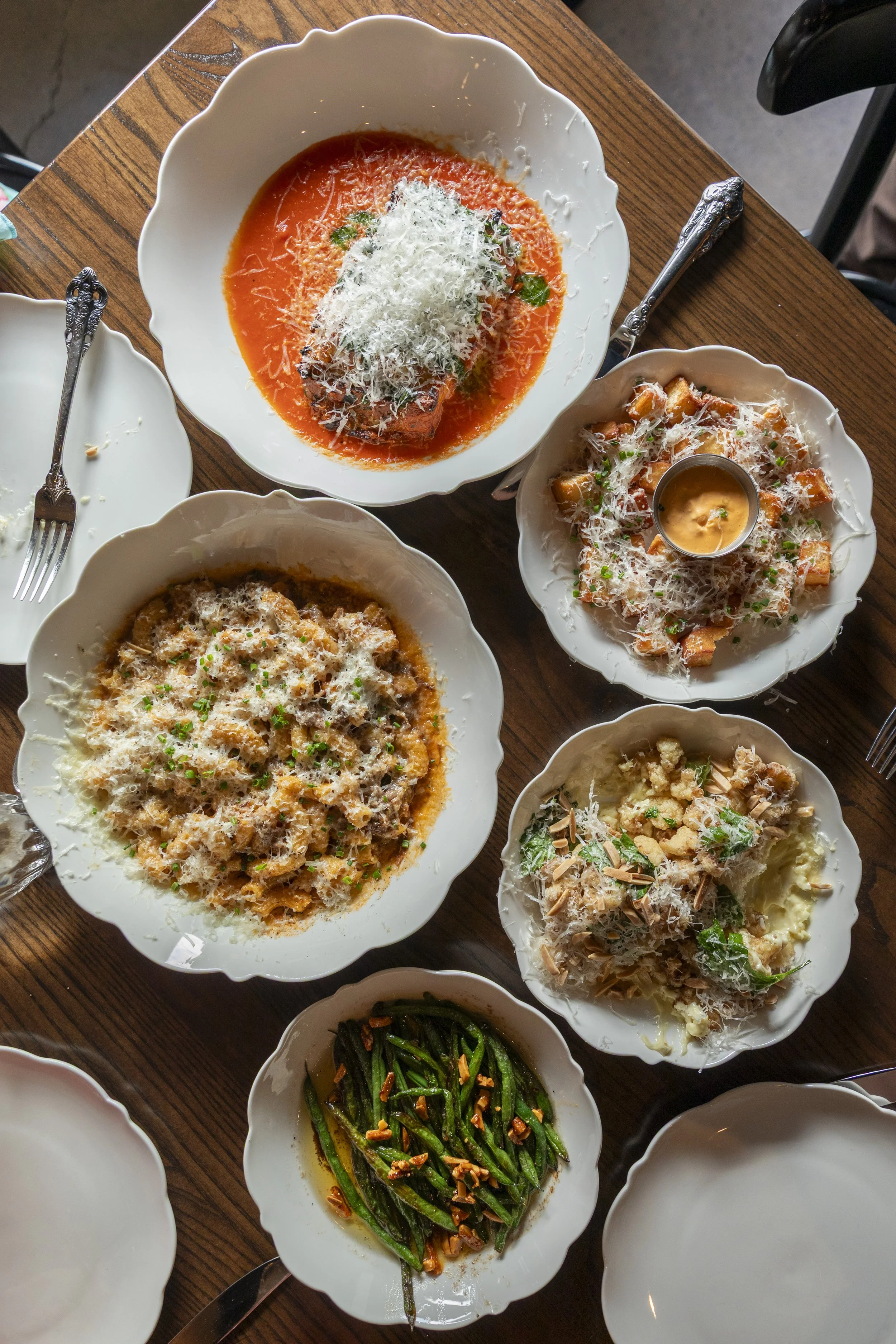 Assorted Italian pasta dishes and a fish dish on a wooden table, topped with grated cheese and herbs.