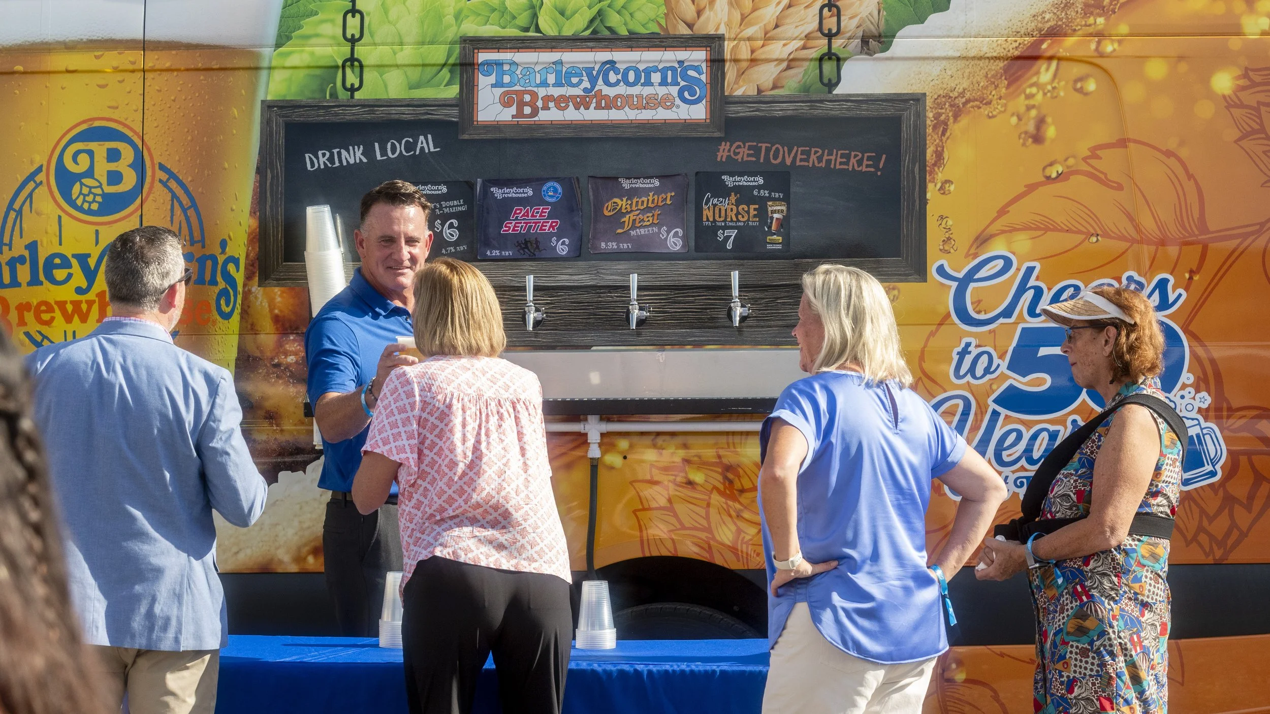 Group of people in line at Barleycorn's Brewhouse food truck, seeking drinks and eating outdoors.