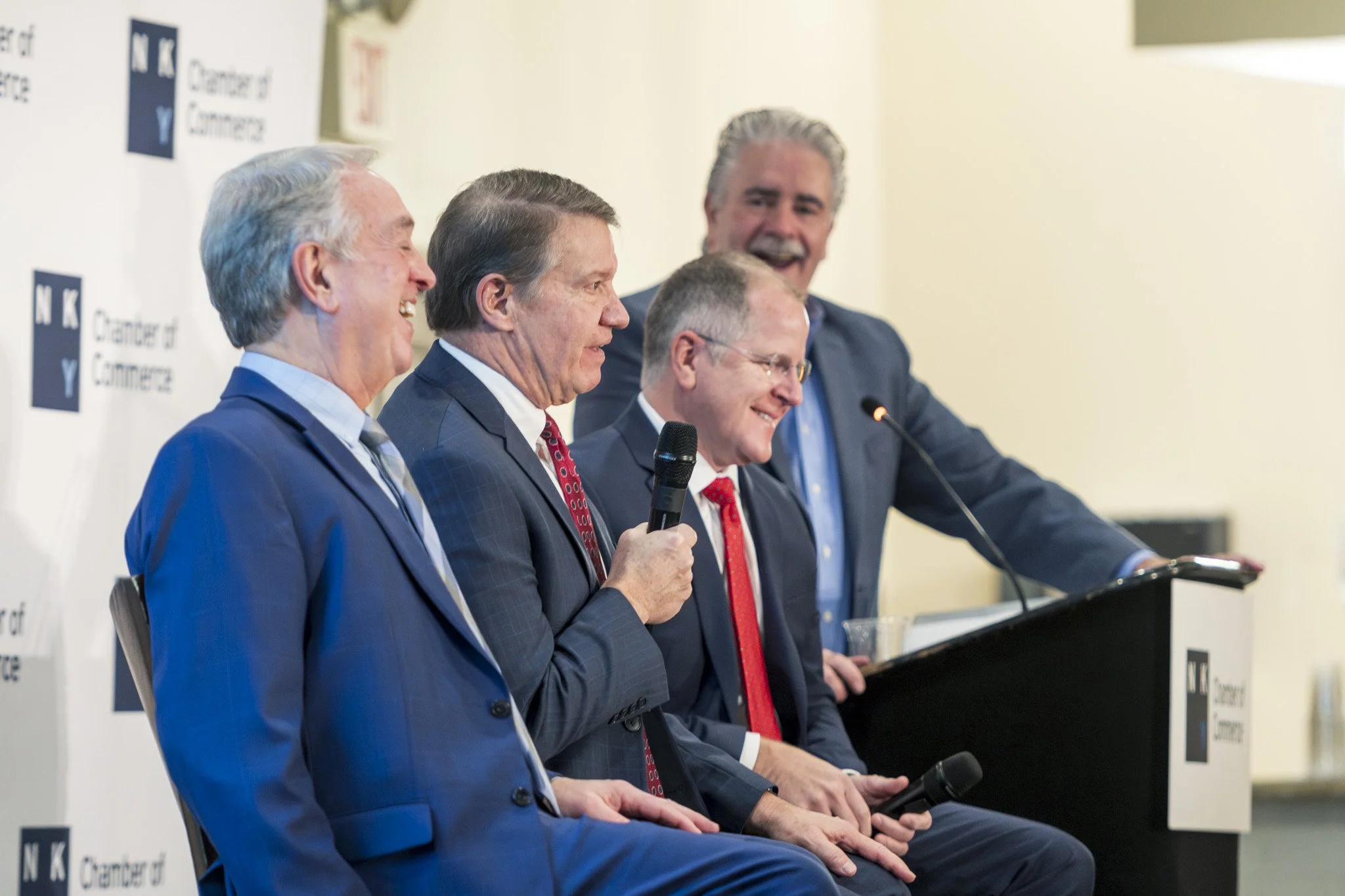 Four men in suits sitting on a stage during a panel discussion at a conference.