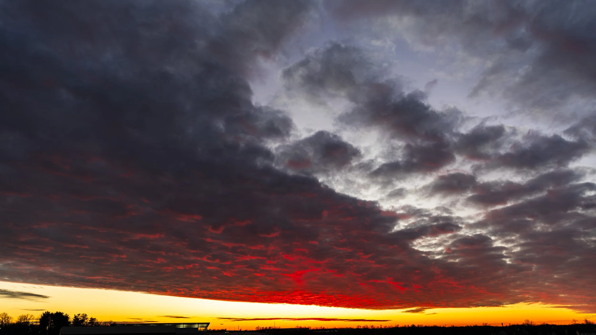 A sunset with dark, dramatic clouds partly illuminated by the orange and yellow glow near the horizon.