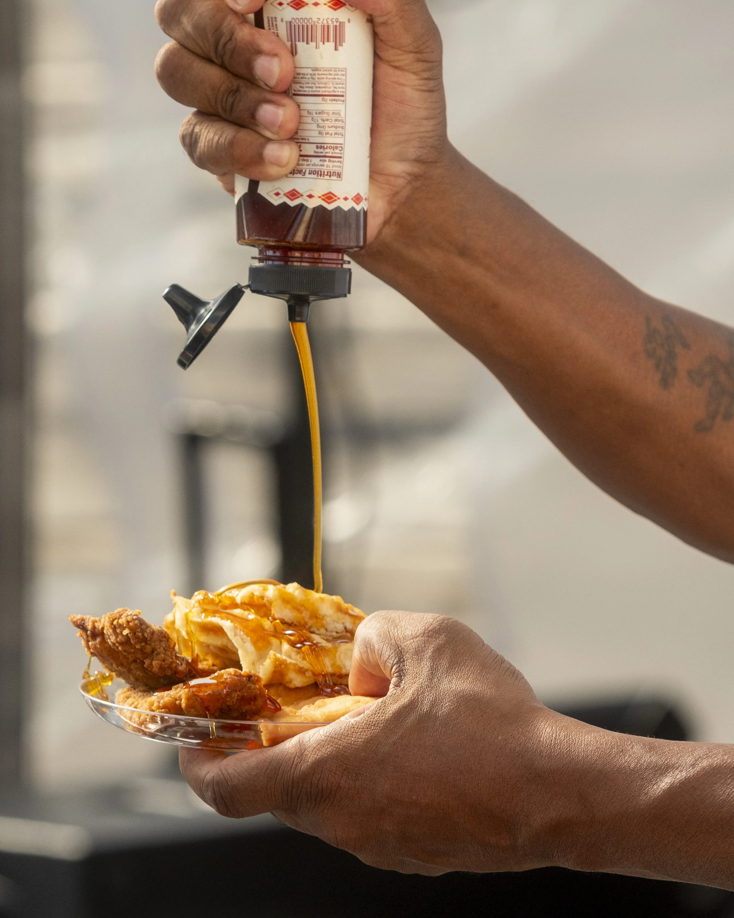 Person pouring ketchup on fried chicken and mashed potatoes with gravy in a plastic dish.
