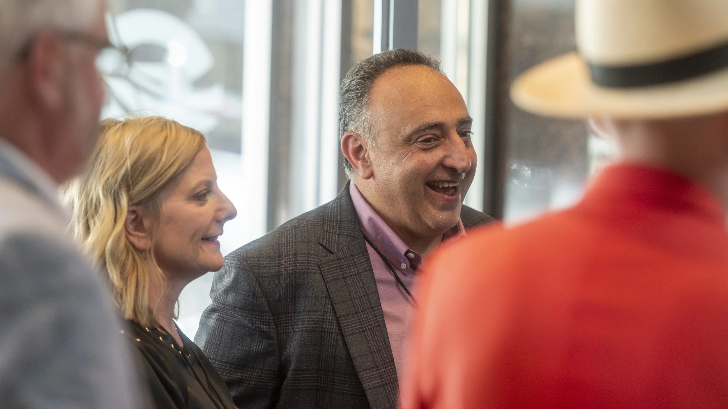 Four people chatting and smiling in a well-lit indoor setting, with two men and two women, dressed in business casual clothes.