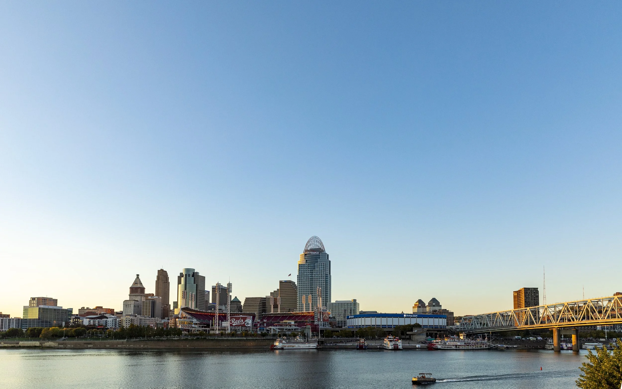 City skyline with high-rise buildings across a body of water, with a bridge on the right side and boats on the water.