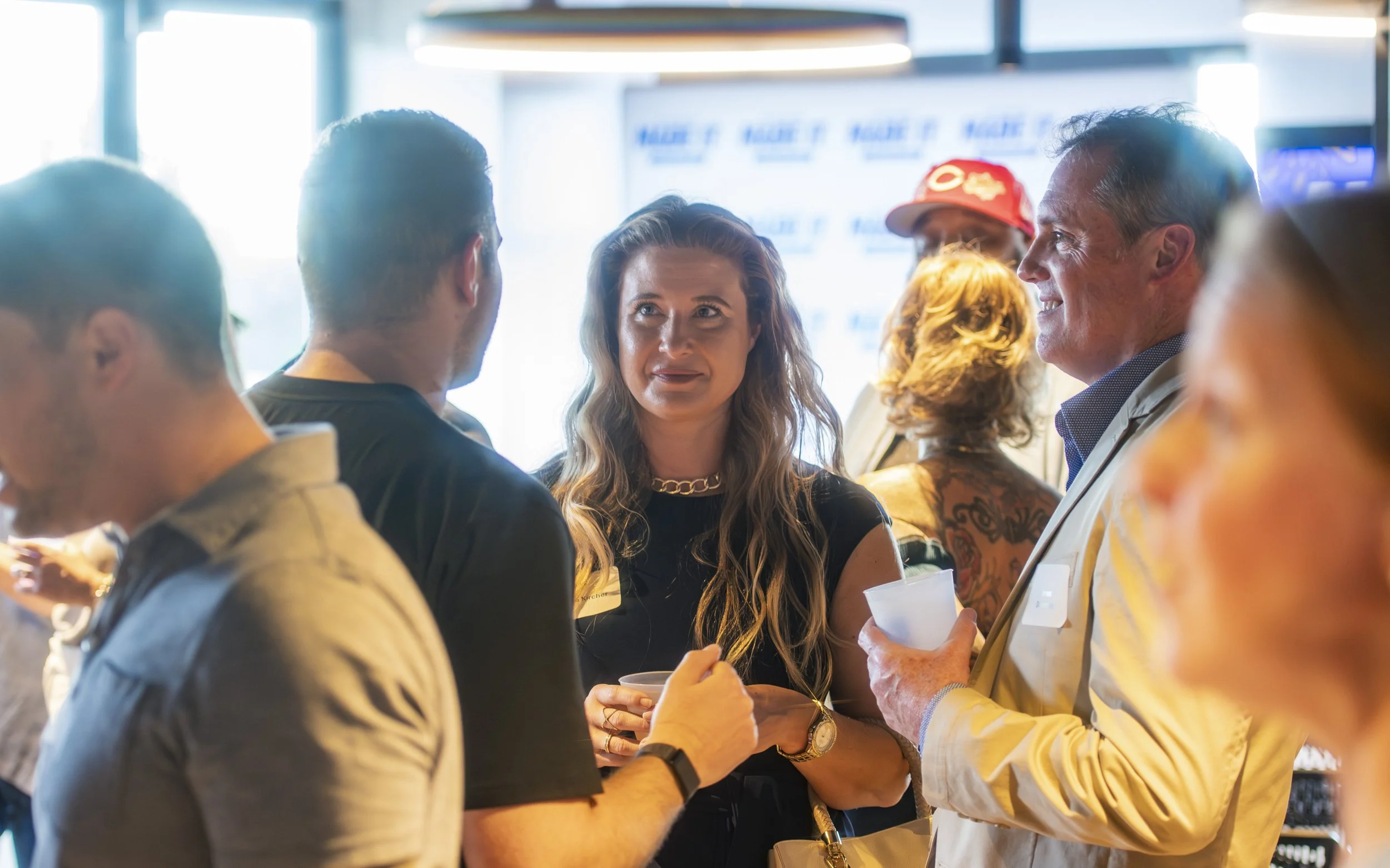 People socializing at an indoor event, with a woman and man in focus holding drinks and engaging in conversation.