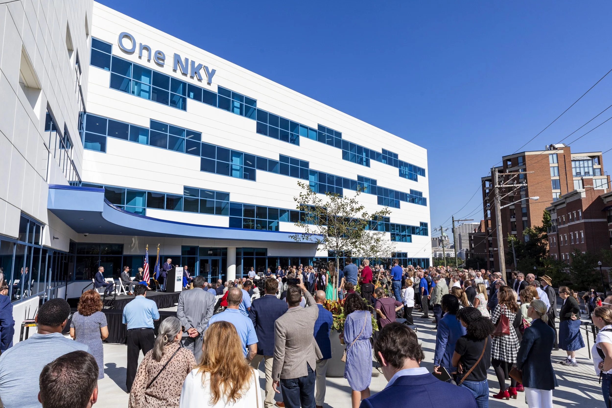 Crowd gathered outside a modern building with a sign that reads 'One NKY' on a sunny day
