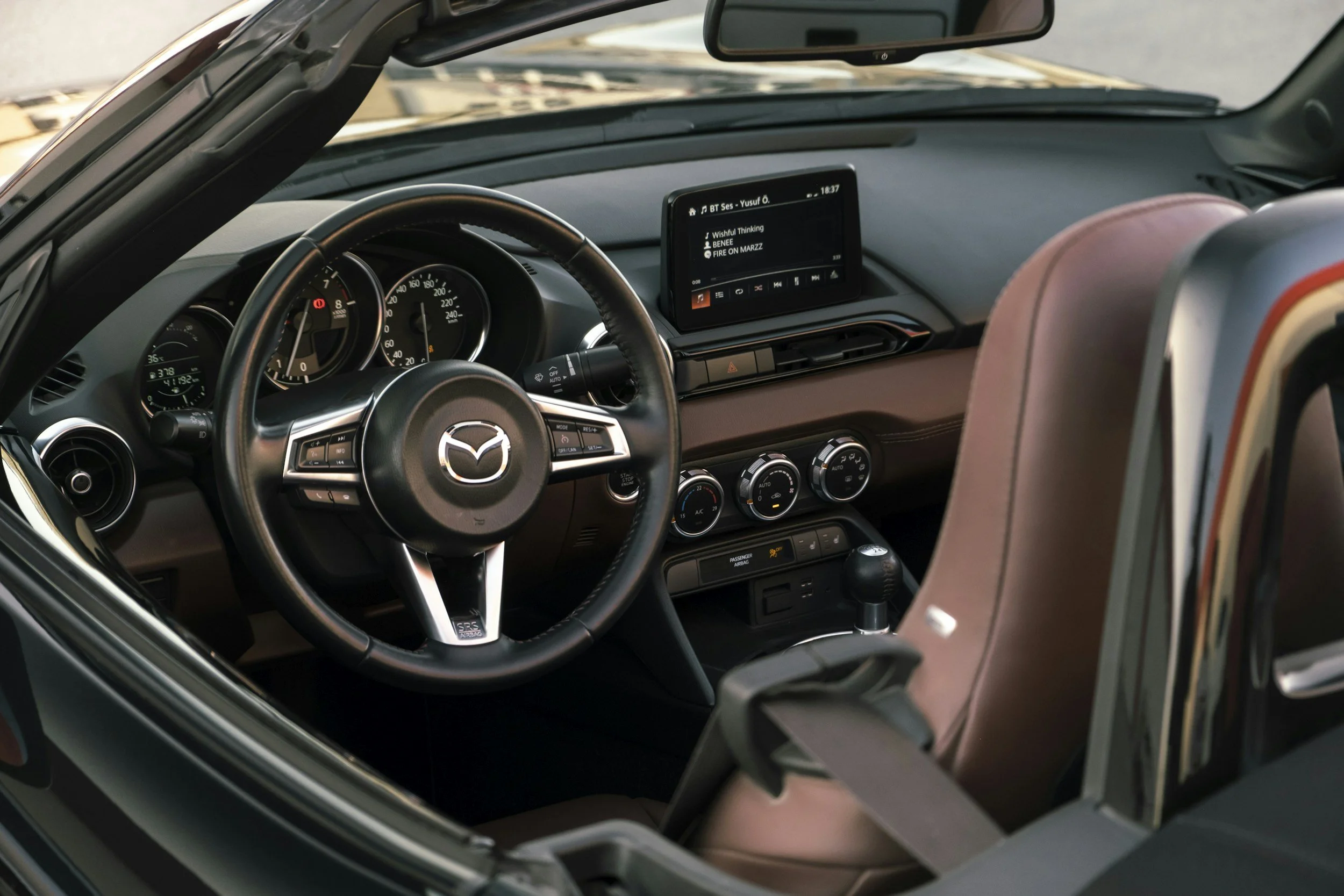 Interiör av en Mazda bil med ratt, instrumentpanel, mittkonsol och en barnstol fram.