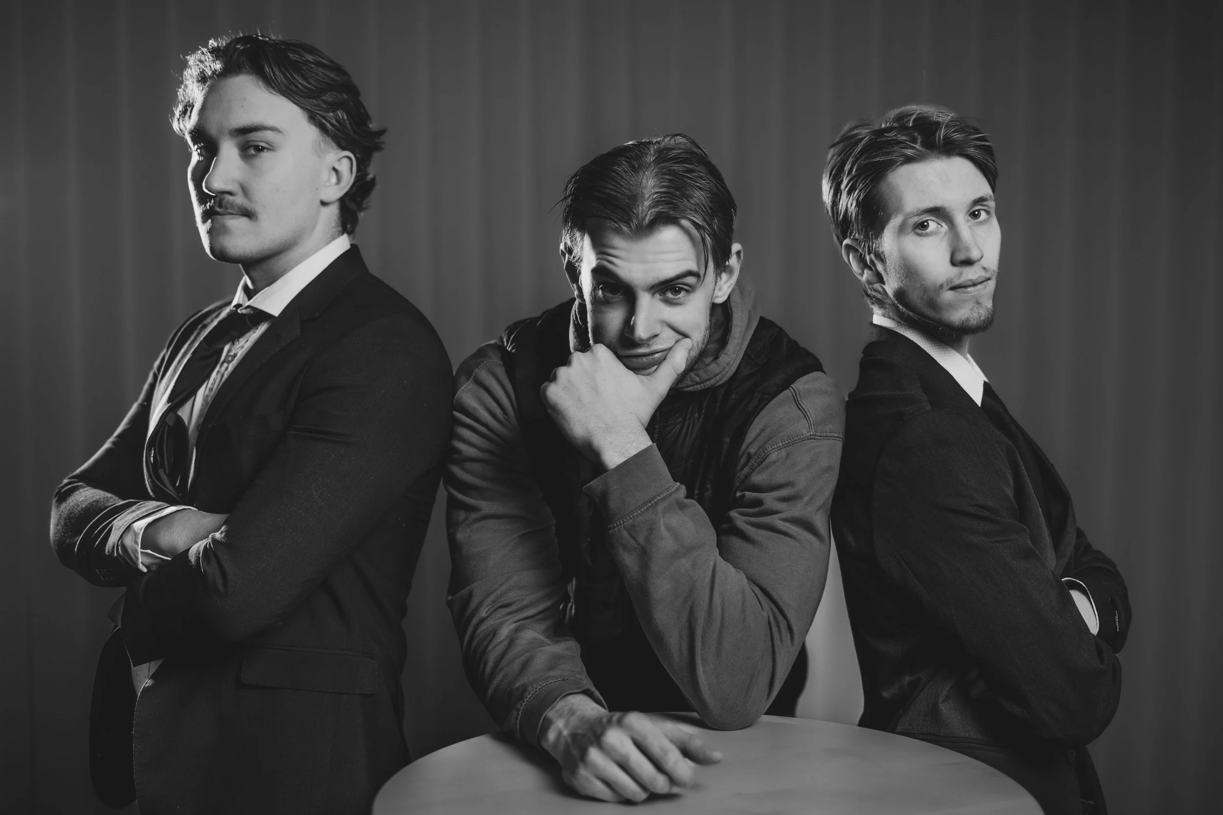 Svartvitt foto av tre unga män som står i rad, med olika poser, mot en enkel bakgrund.