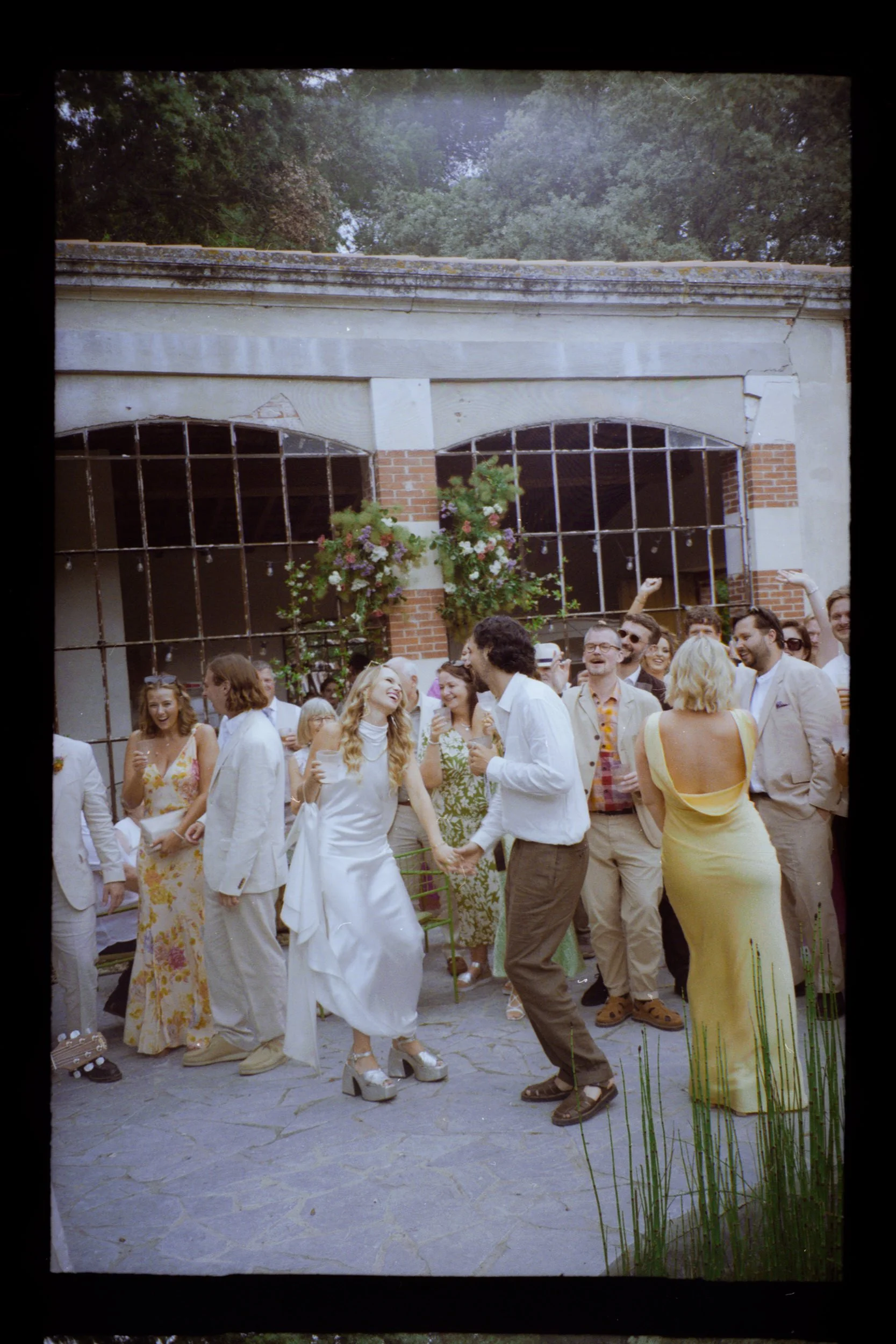 Photo argentique couleur des mariés anglais dansant lors du cocktail de leur mariage à La Belle Eco dans le sud-ouest de la France. La mariée stylée et chic porte une robe alternative The Own Studio London et chaussures argent à plateforme Nodaleto