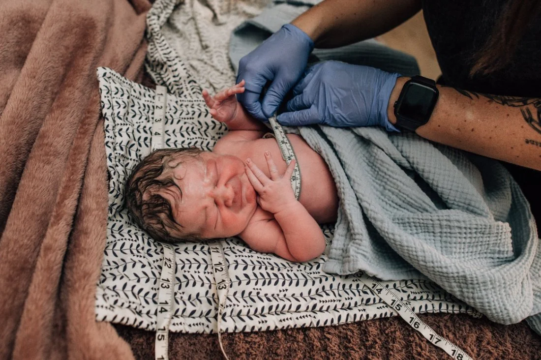 Newborn baby receiving gentle measurements after a Home Birth, surrounded by family in a calm home setting