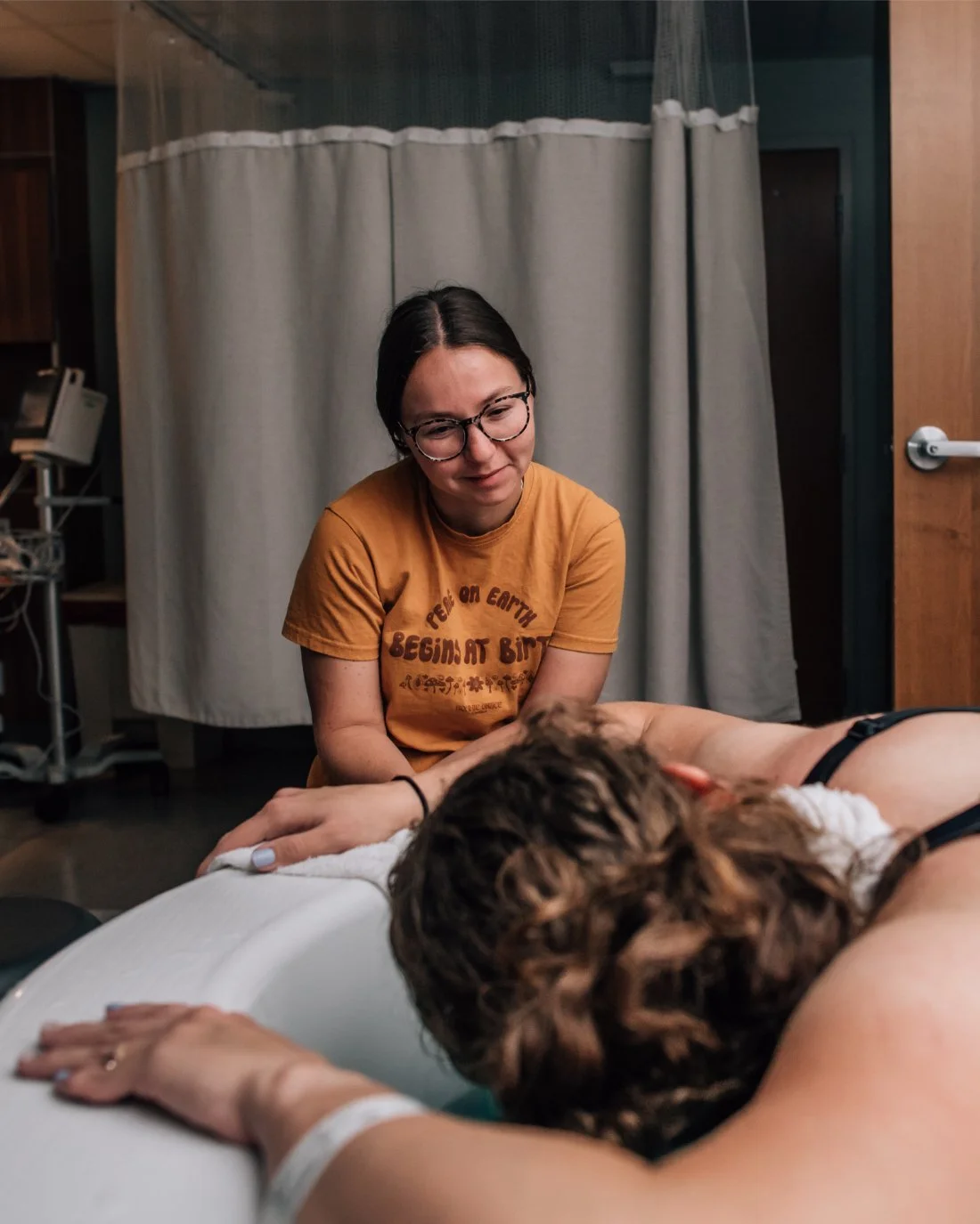 Laboring parent leaning over a birth tub while doula stays nearby, demonstrating attentive presence and compassion central to becoming a doula.