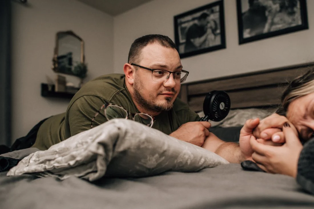 Partner offering quiet support during labor while holding the birthing parent’s hand, a moment often remembered through childbirth photography.