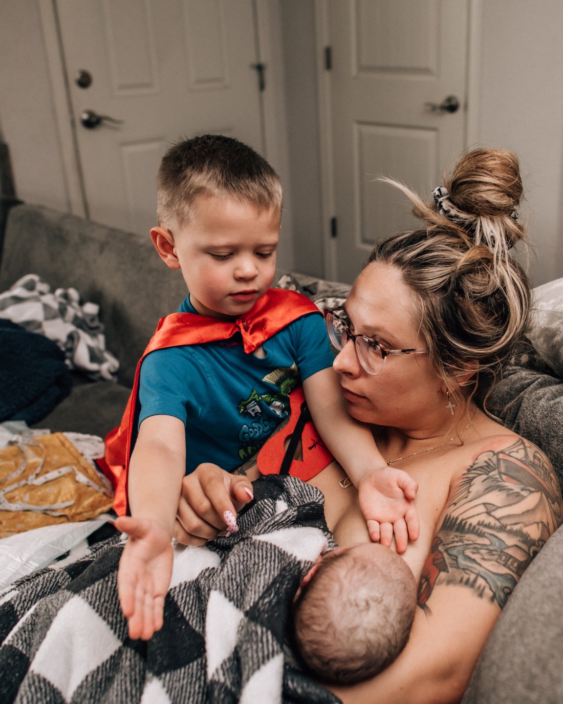 Parent holding newborn while an older sibling looks on with curiosity, showing how childbirth photography captures the beginning of family connection.
