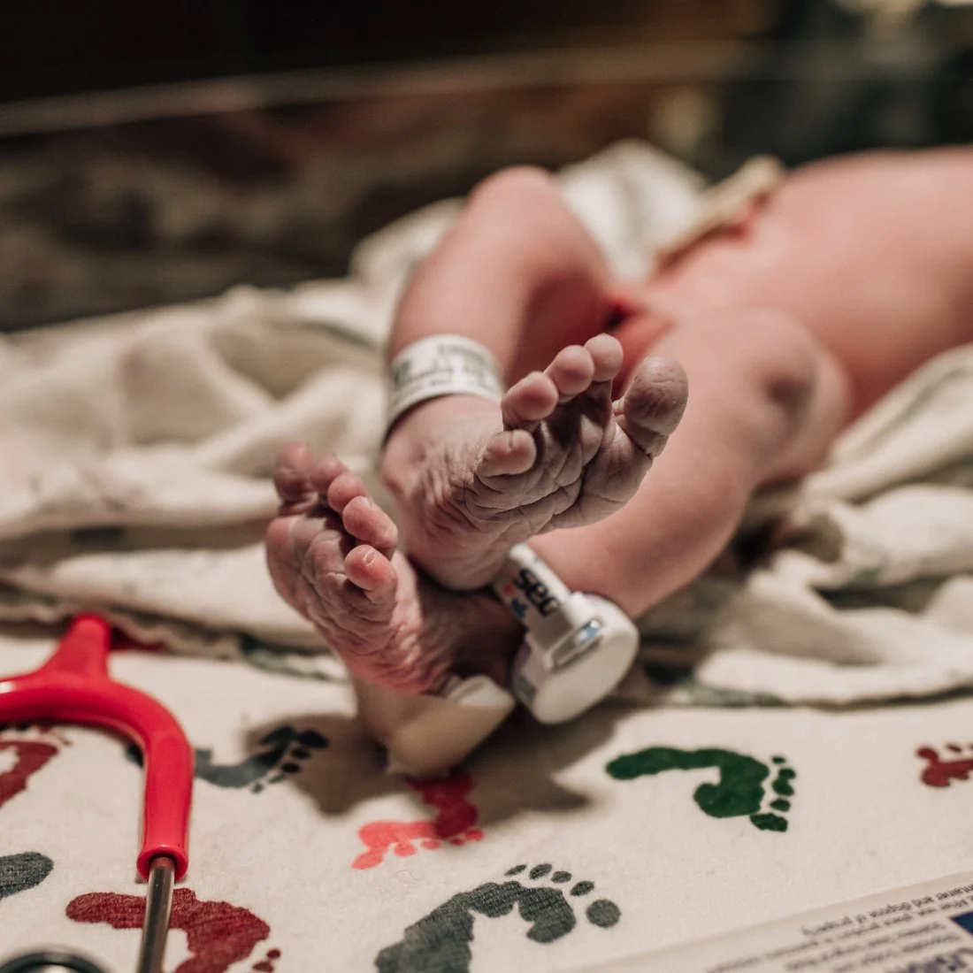Close up of newborn feet resting on a hospital blanket with identification bands, highlighting early newborn moments preserved through childbirth photography.