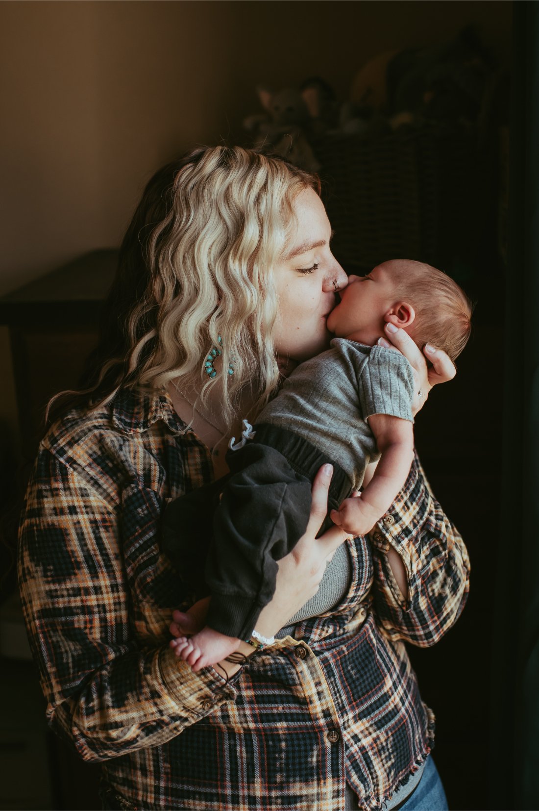 Parent kissing their newborn’s forehead while standing in window light, an example of connection focused natural newborn photography.