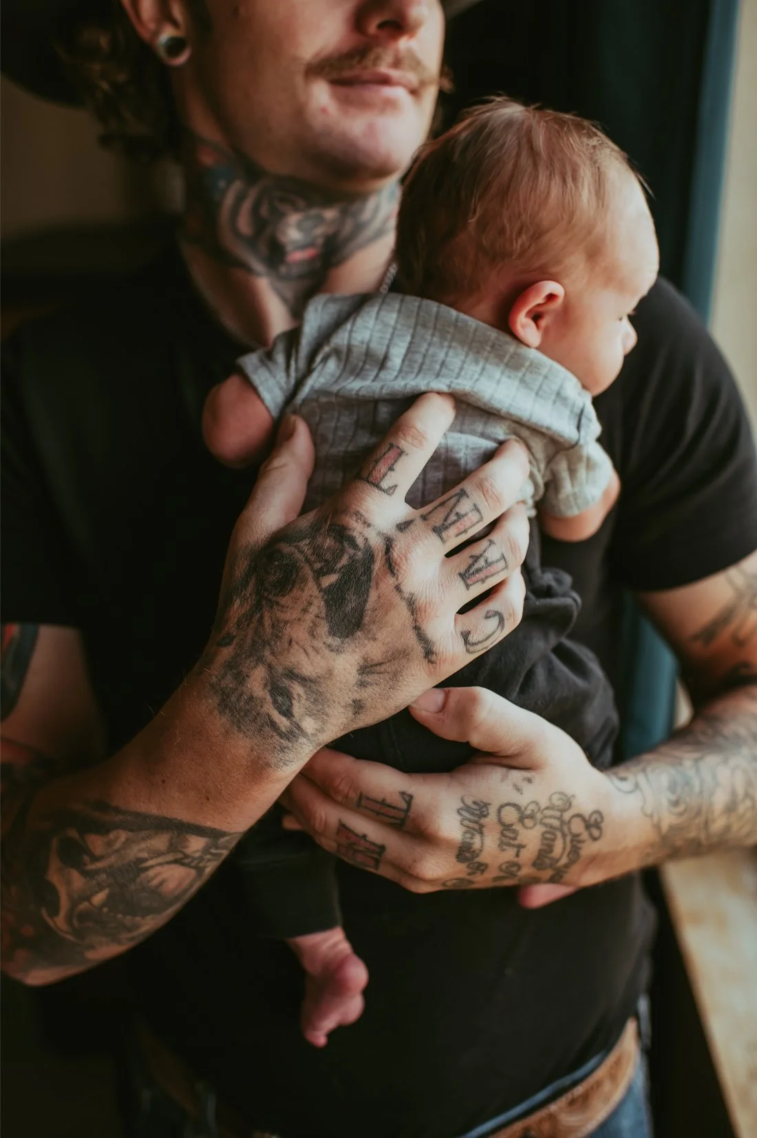 Tattooed parent holding their newborn against their chest, photographed candidly during a natural newborn photography session.