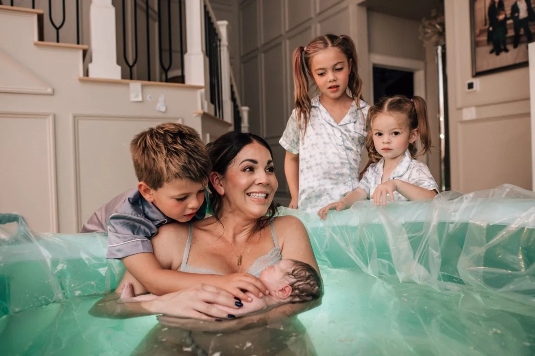 Mother holding newborn baby after a Home Birth while siblings look on in quiet amazement and connection