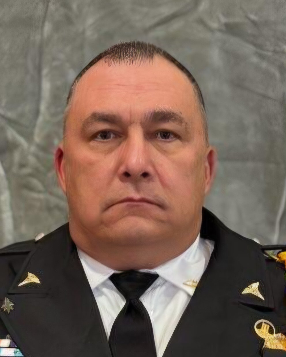 A man in a military uniform with a serious expression, short dark hair, and a decorated shoulder patch.