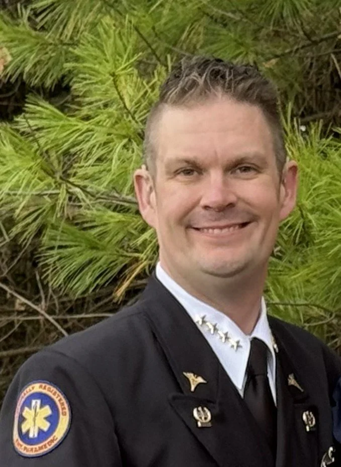 Smiling man in white polo shirt with logo against black background.