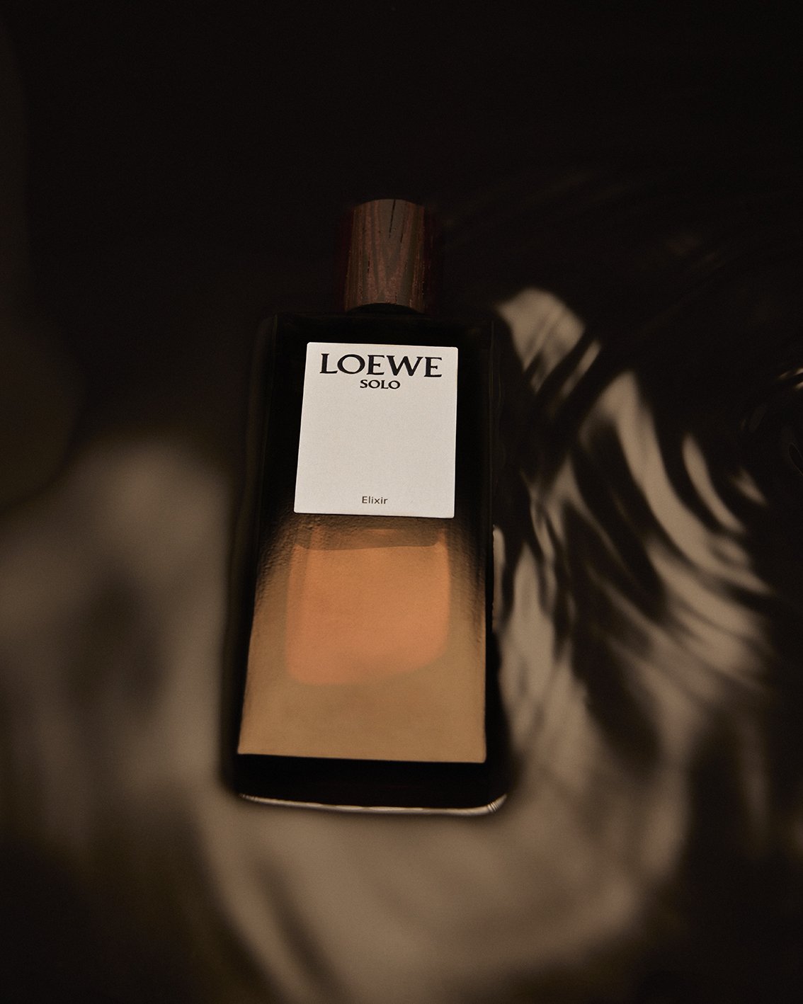 A bottle of Loewe Solo Elixir cologne inside a dark bag with a striped fabric lining.