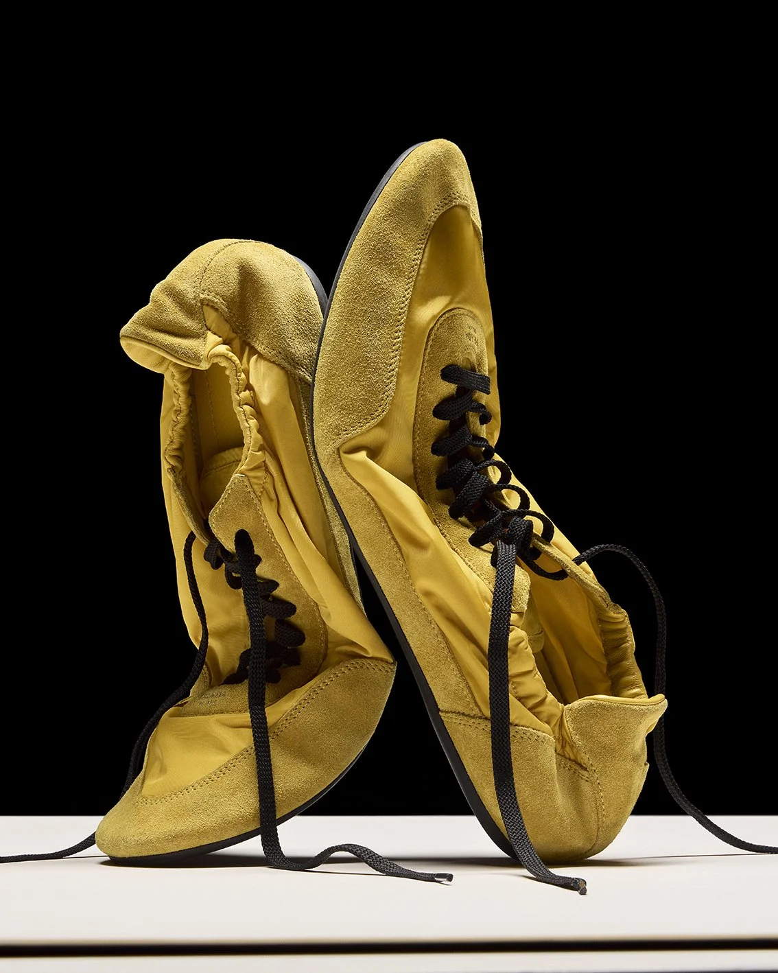 Pair of yellow sneakers with black laces displayed against a black background.