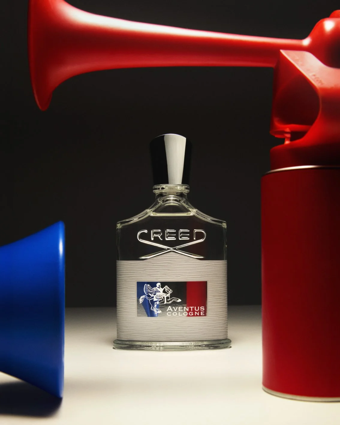 Luxury Creed Fragrance framed between a red and blue horn in a studio setting.