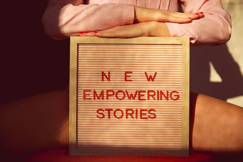 Bacheca di legno con lettere rosse che compongono 'New Empowering Stories', tenuta tra le mani di una persona