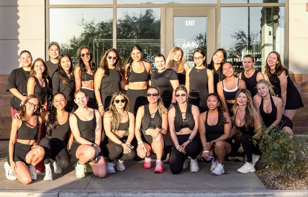 Group of women wearing black athletic clothing, posing outside of Solidity Studio, in the sunlight. Grace Run Club 2 year anniversary event with Solidity Studio.