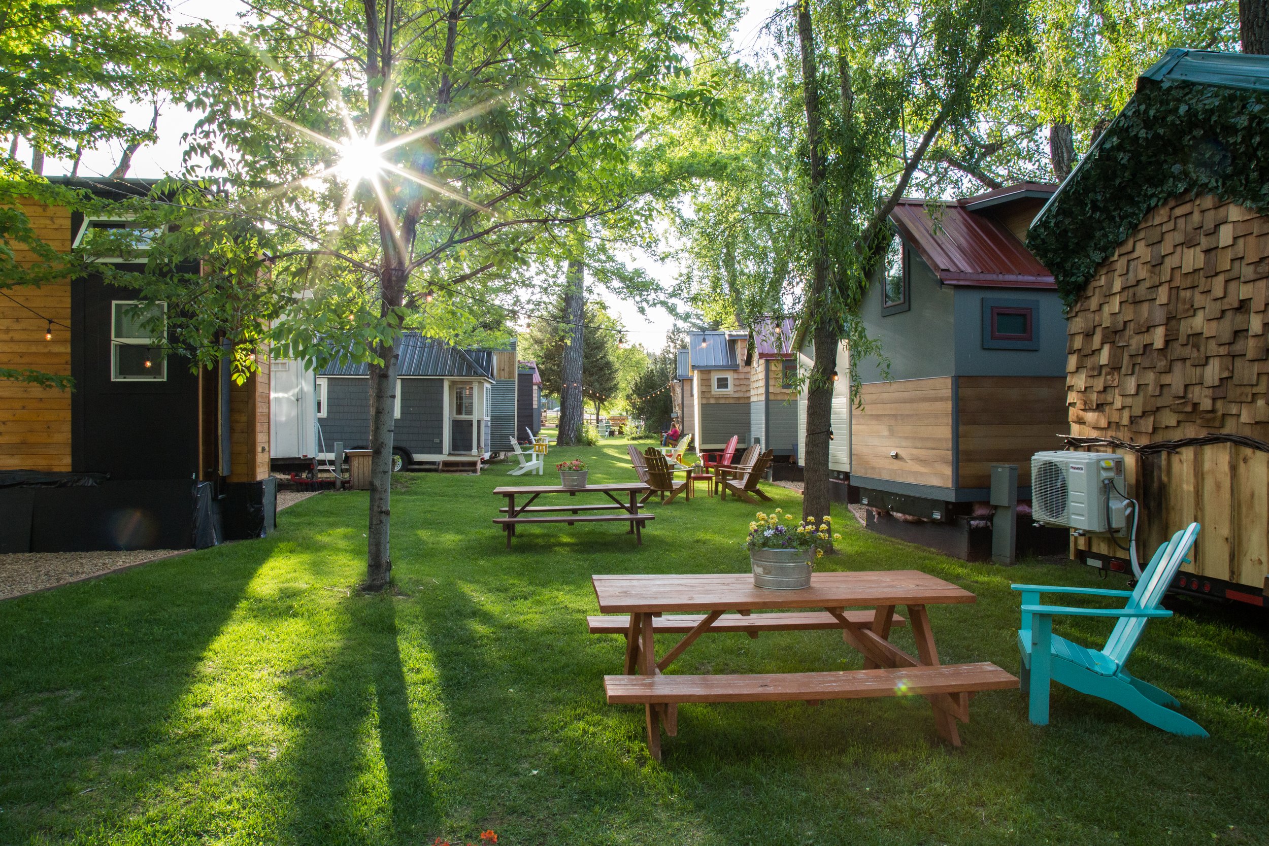 Rows of tiny houses surround a lush green yard populated with seating areas and picnic tables, the perfect space for groups to connect outdoors.