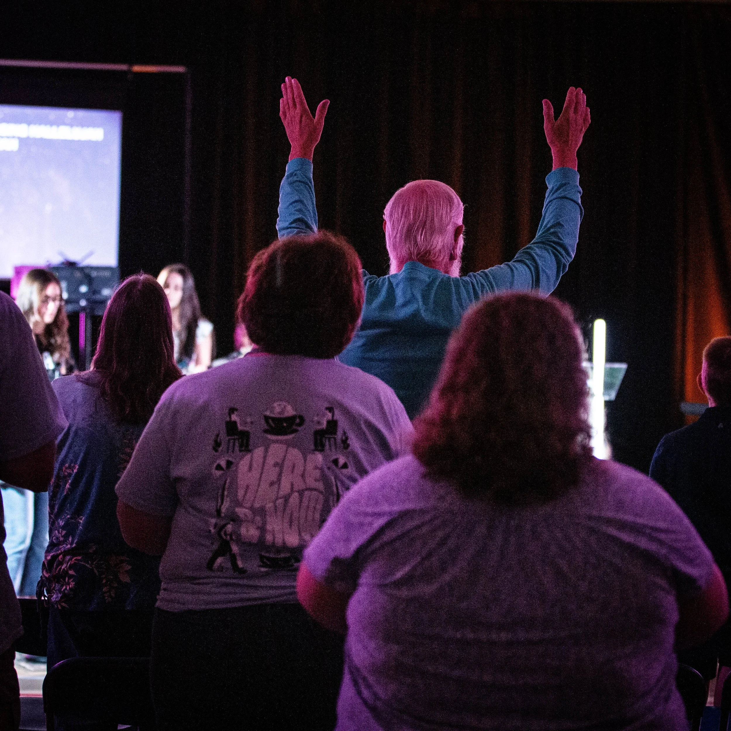 Group of people attending a presentation or conference, with one man raising his hands.