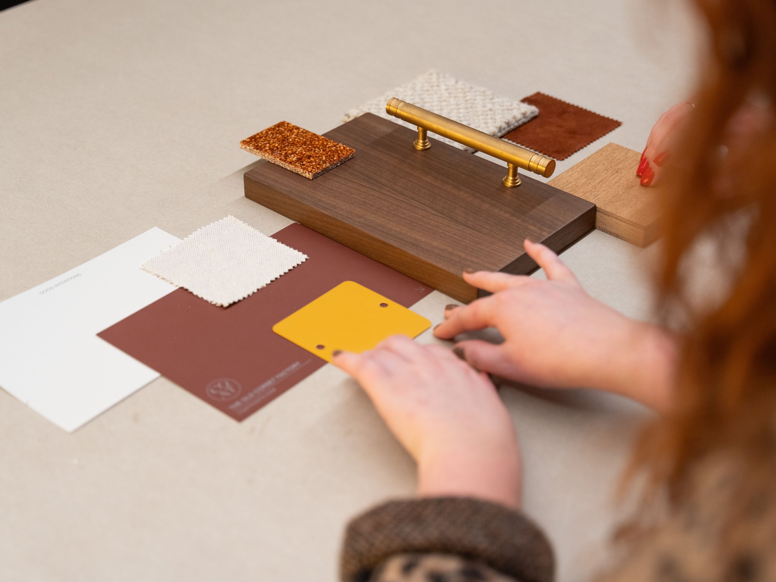Person examining color and material samples laid out on a table, including fabric swatches, color chips, and wood finish options.