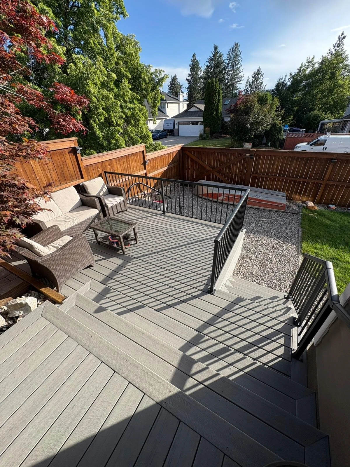View of a backyard patio with outdoor furniture, a wooden deck, a gravel area, and a wooden fence, under clear blue skies.