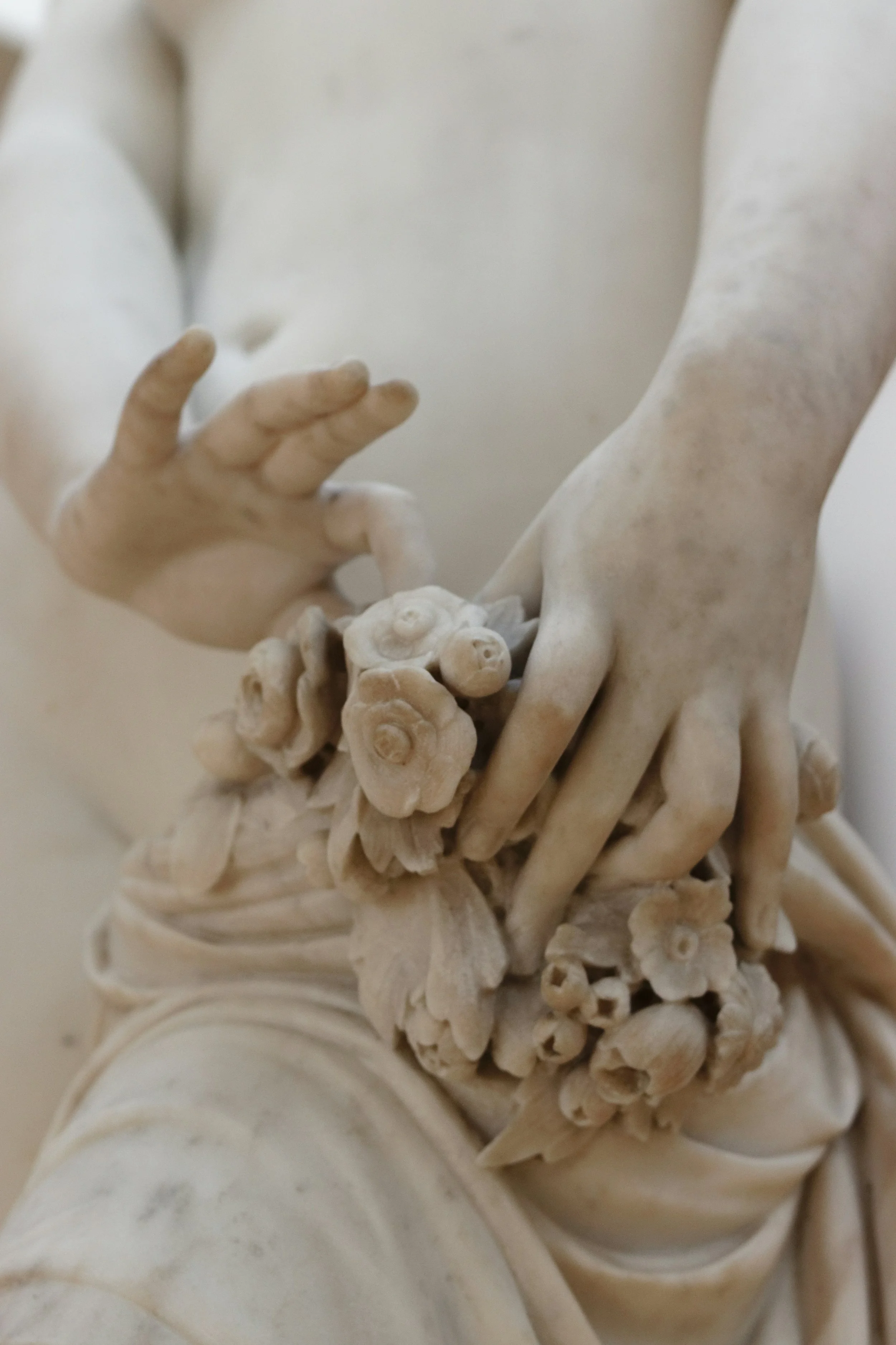 Close-up of a marble sculpture depicting two hands, one gently touching the other, with detailed flowers and fabric carved around the hands.