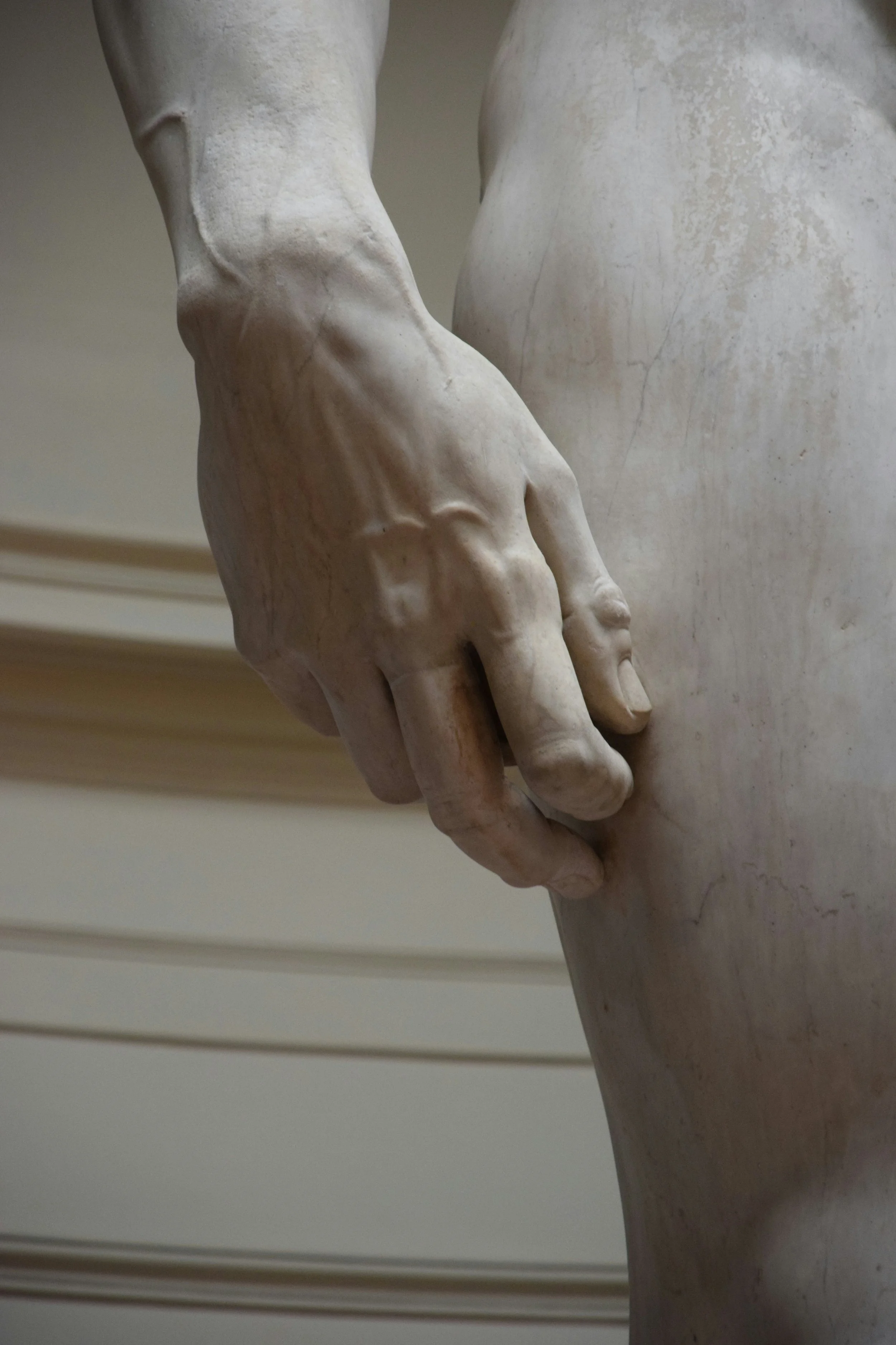 Close-up of a white marble statue depicting a human hand and part of the torso.