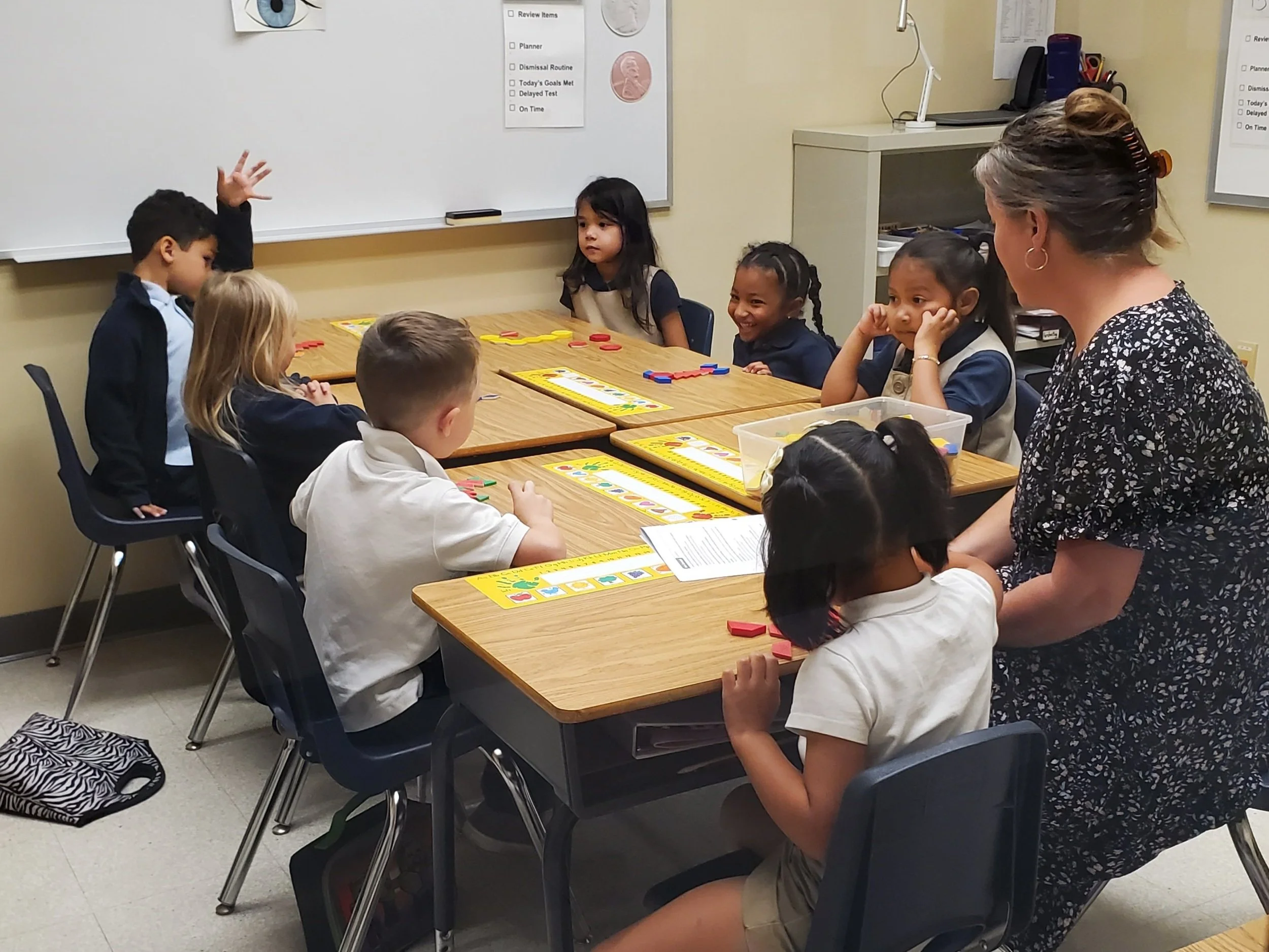 Teacher and young students in a classroom playing a board game at a table.