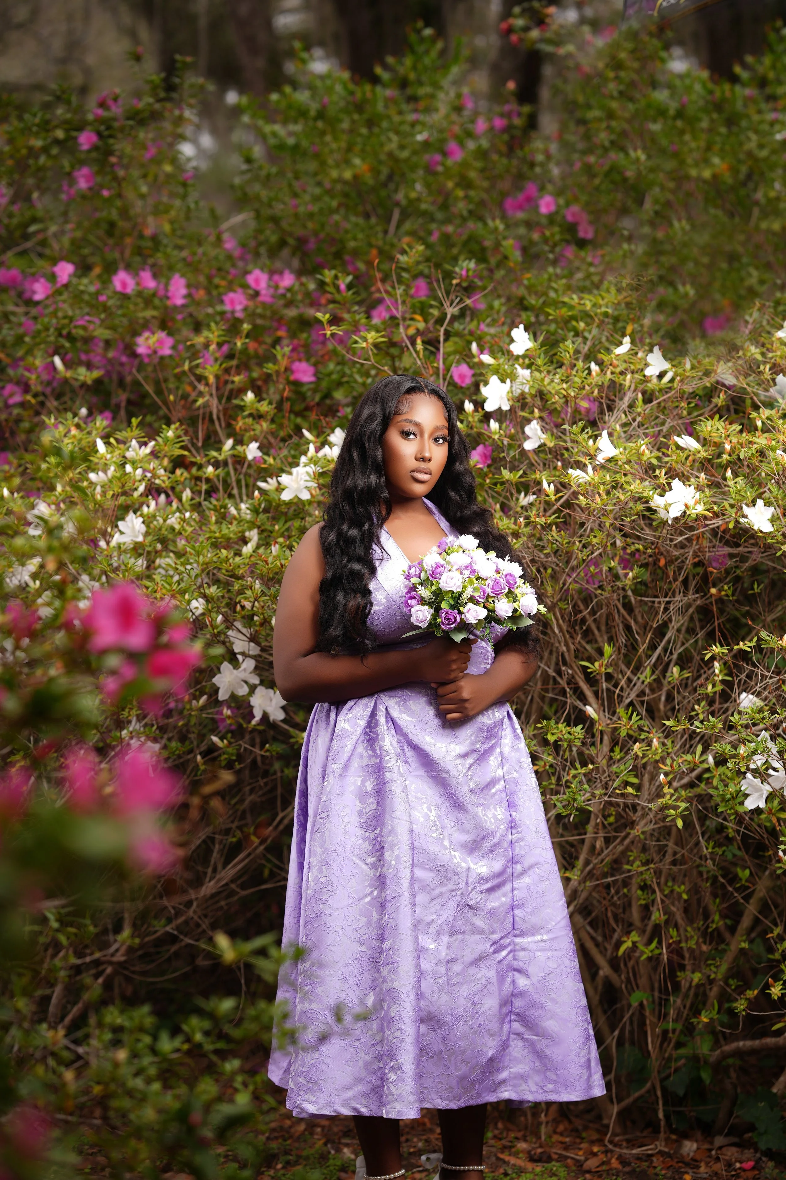 A young woman with long black hair in a purple dress holding a bouquet of white and purple flowers, standing among blooming white and pink azaleas.