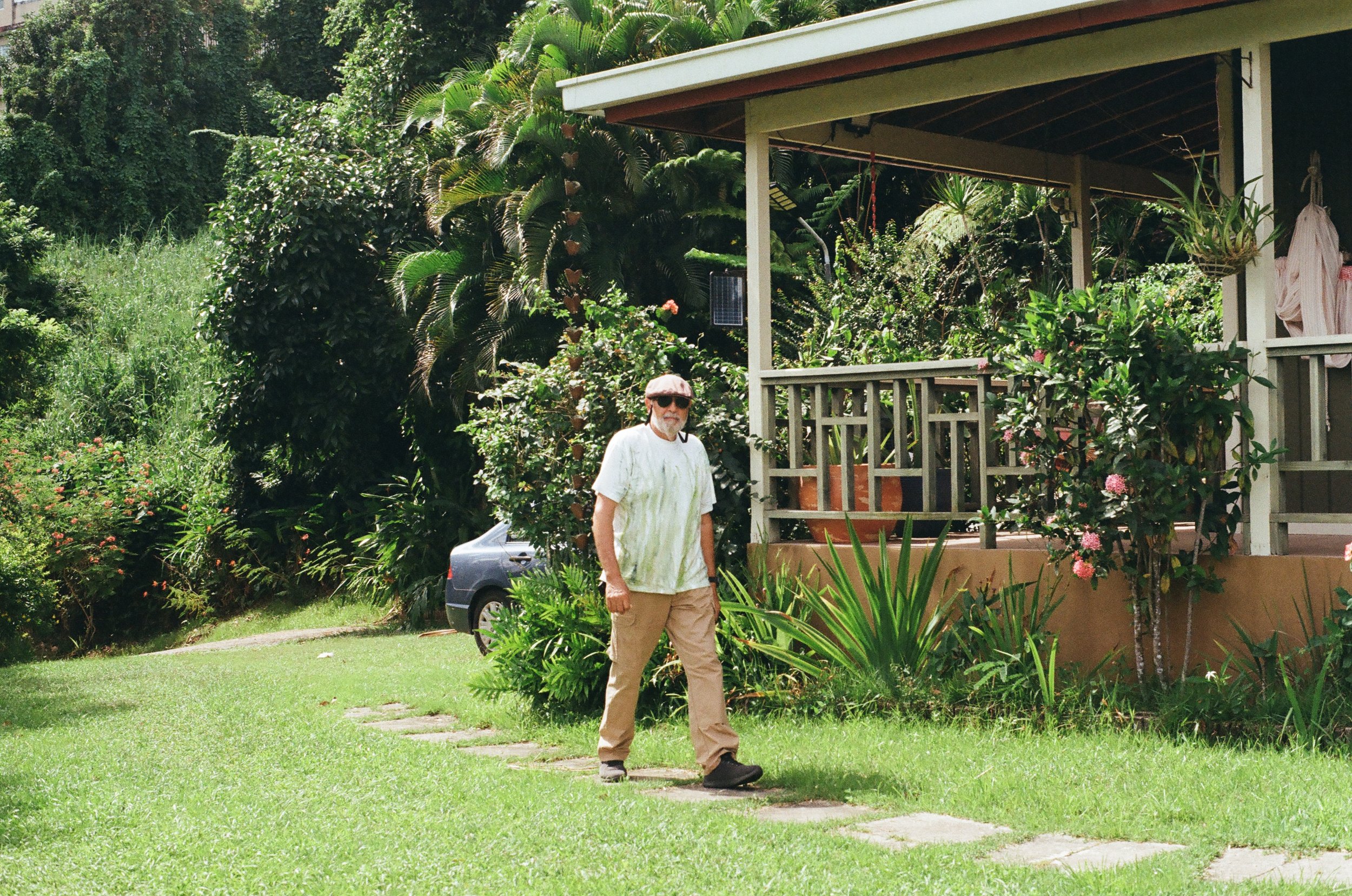 Man walking on a garden path next to a house with lush greenery and plants