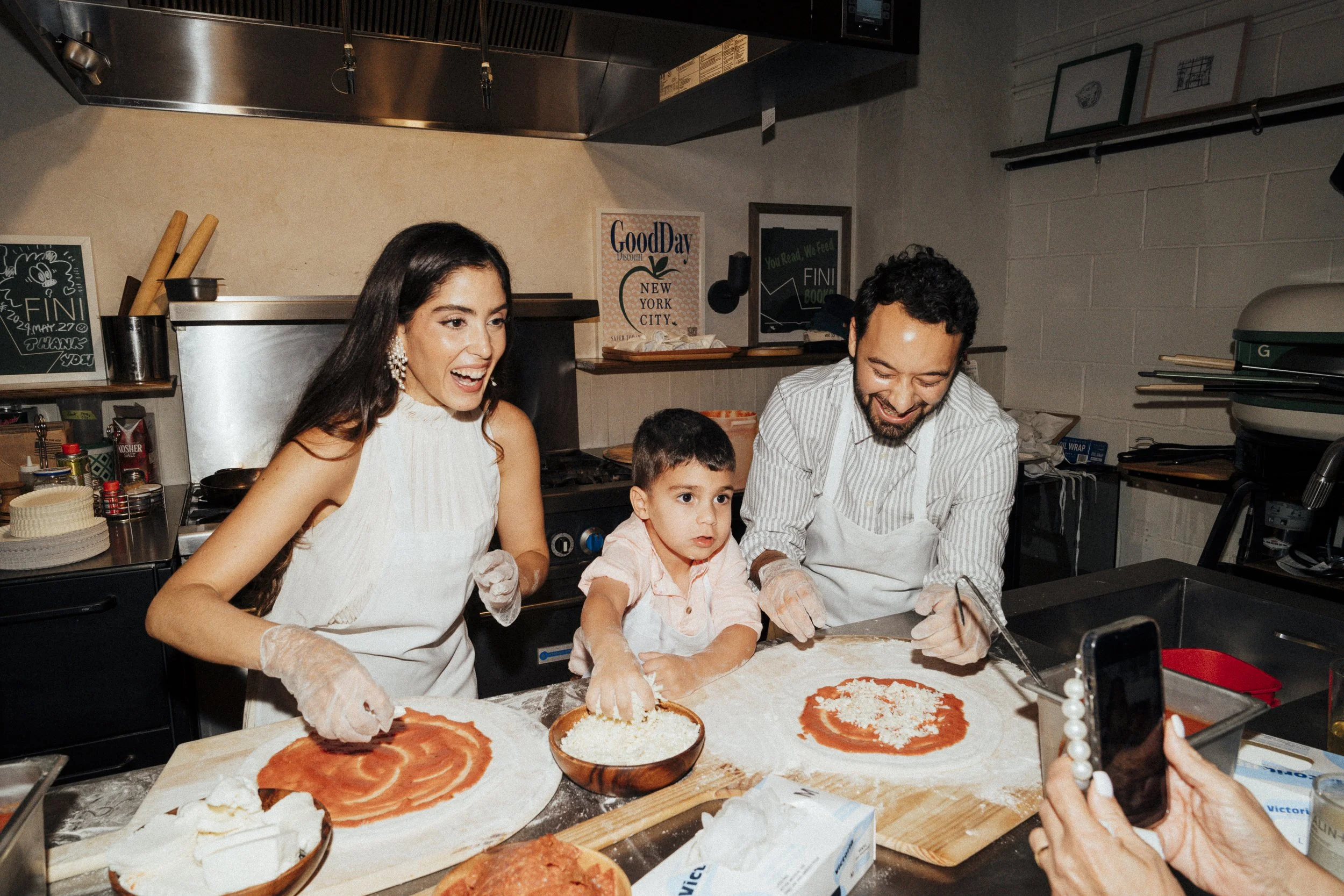 Family making pizza together in a kitchen, using tomato sauce and cheese at Fini Pizza in Brooklyn, NY
