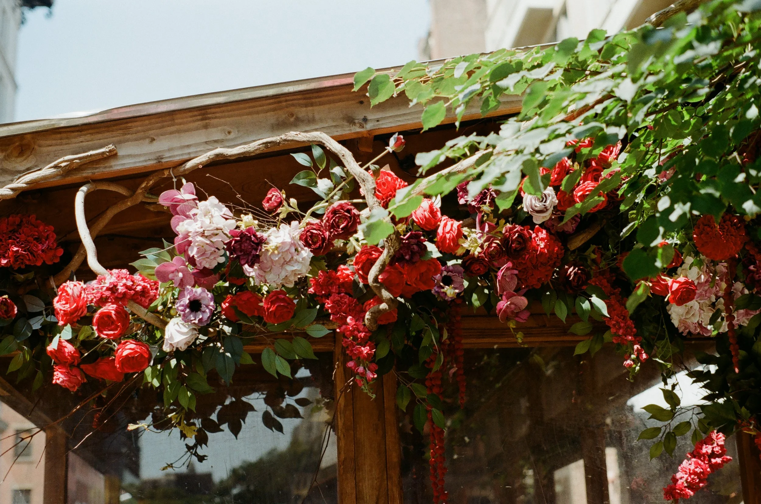Decorative floral arrangement with red, pink, and purple flowers on wooden structure, surrounded by greenery.