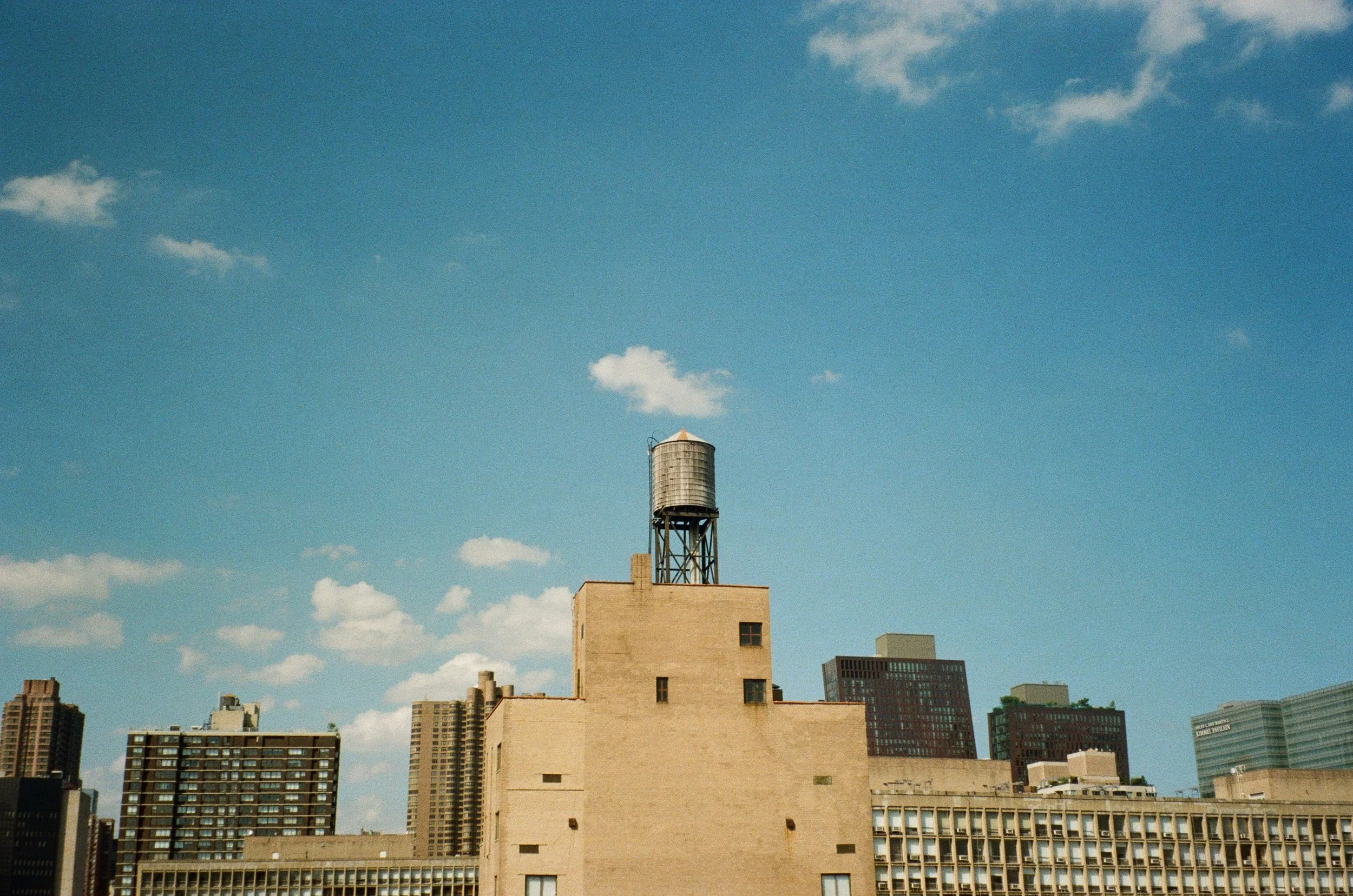 Urban skyline with a water tower on a rooftop under a blue sky.