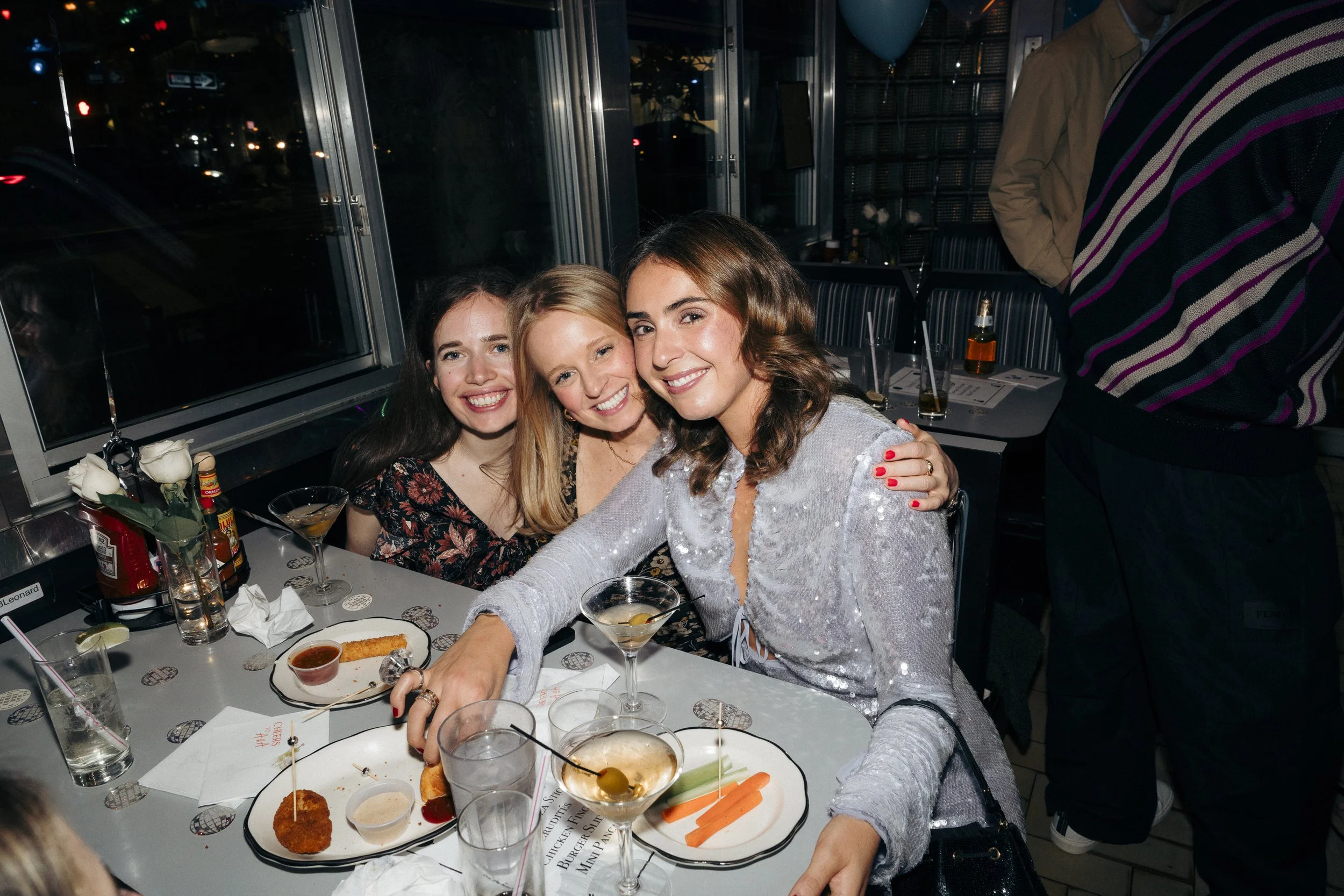 Three women smiling at a restaurant table with drinks and food, including martinis and appetizers Square Diner in New York City