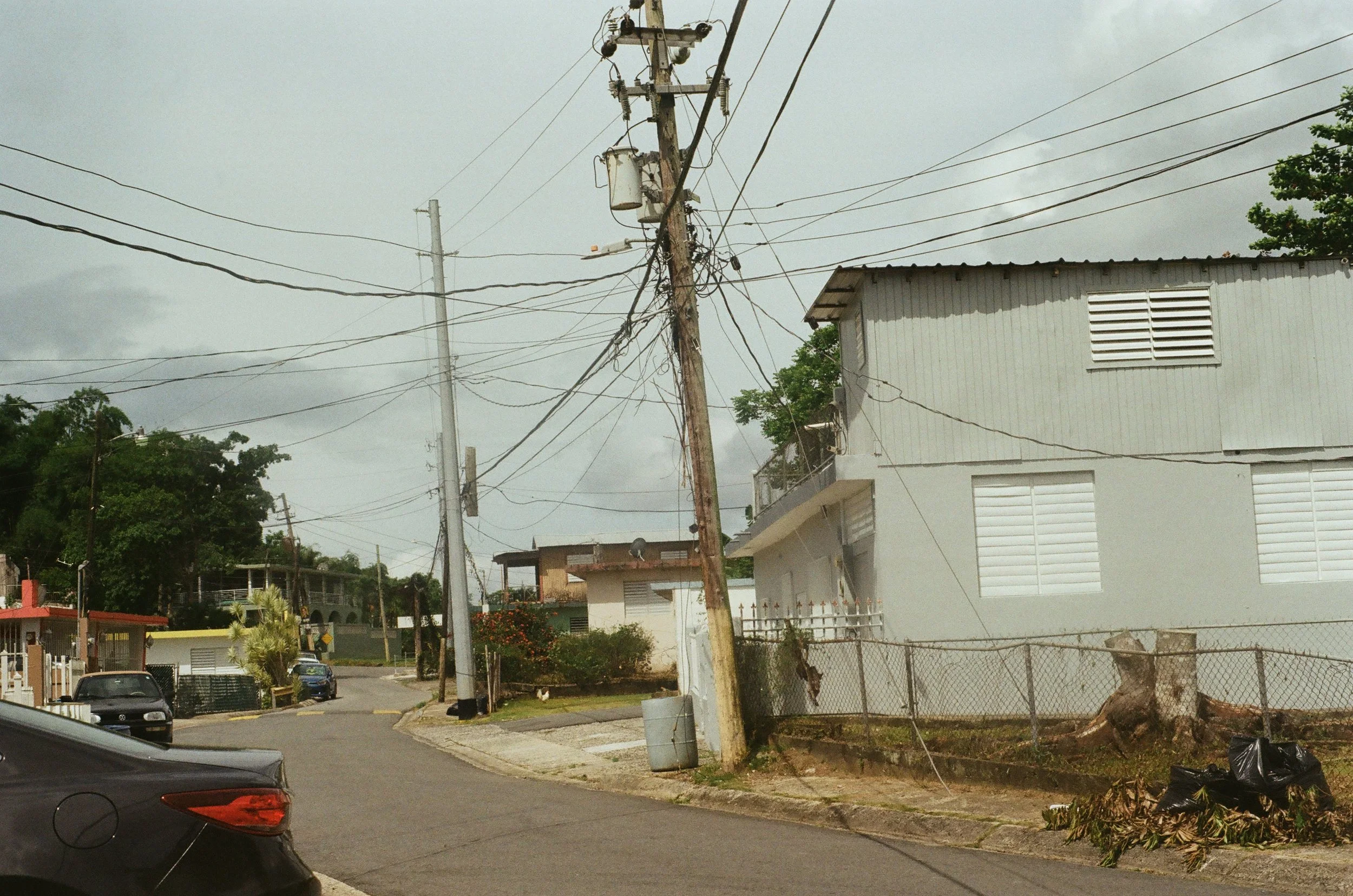 Suburban street with power lines, residential buildings, and parked cars.