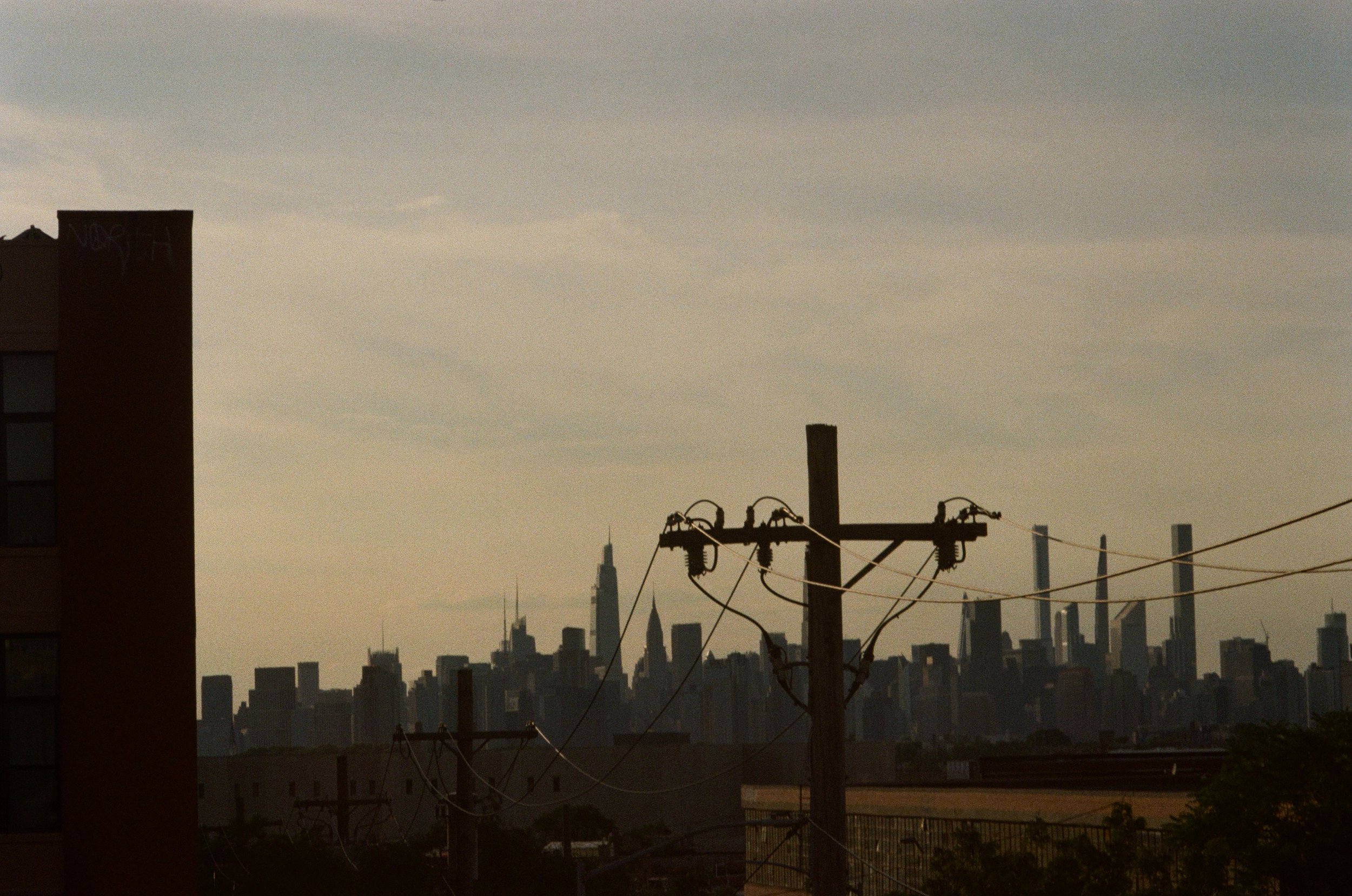 Silhouette of city skyline with power lines and building in foreground.